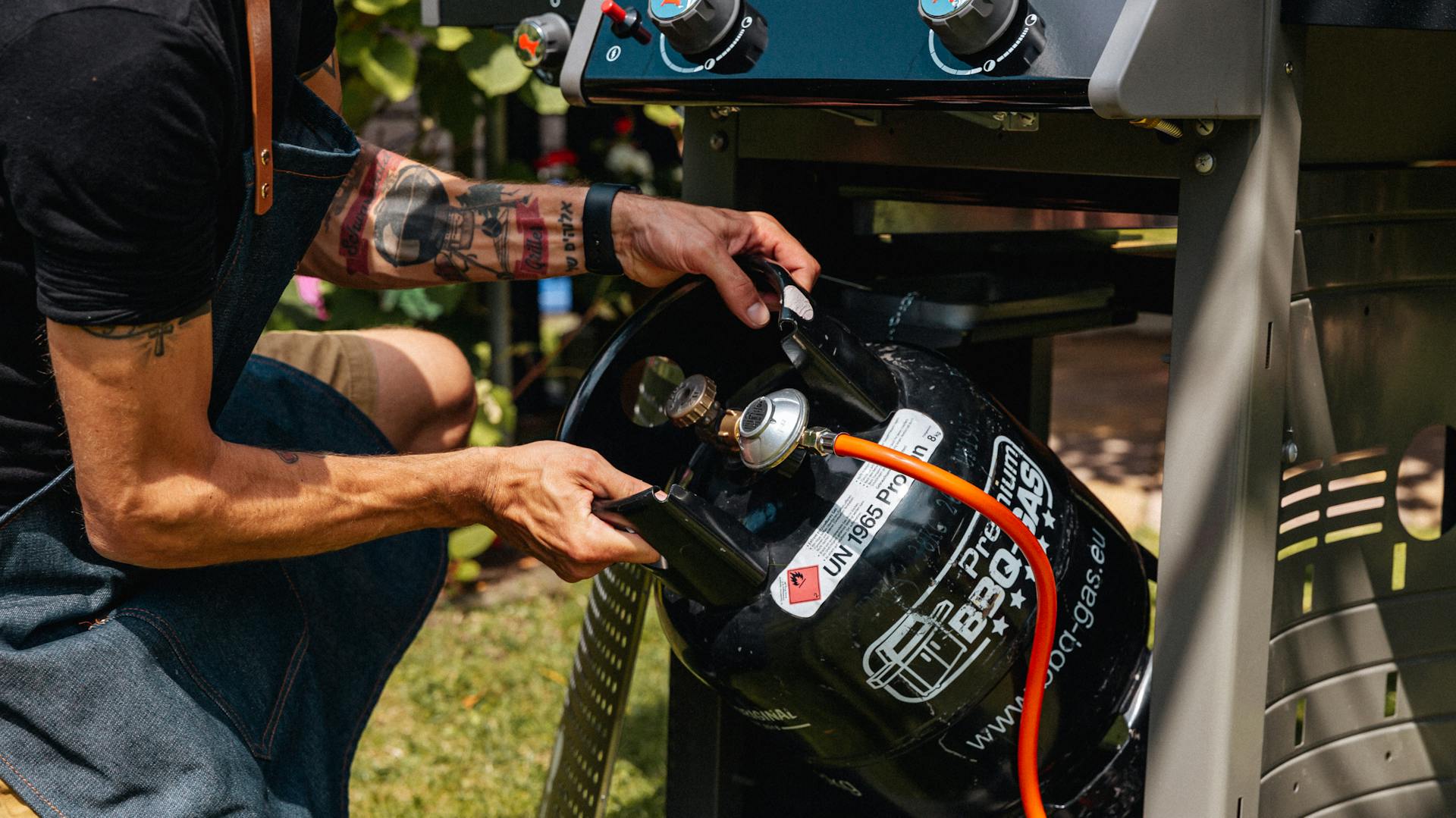 Mann stellt angeschlossene Gasflasche unter Gasgrill
