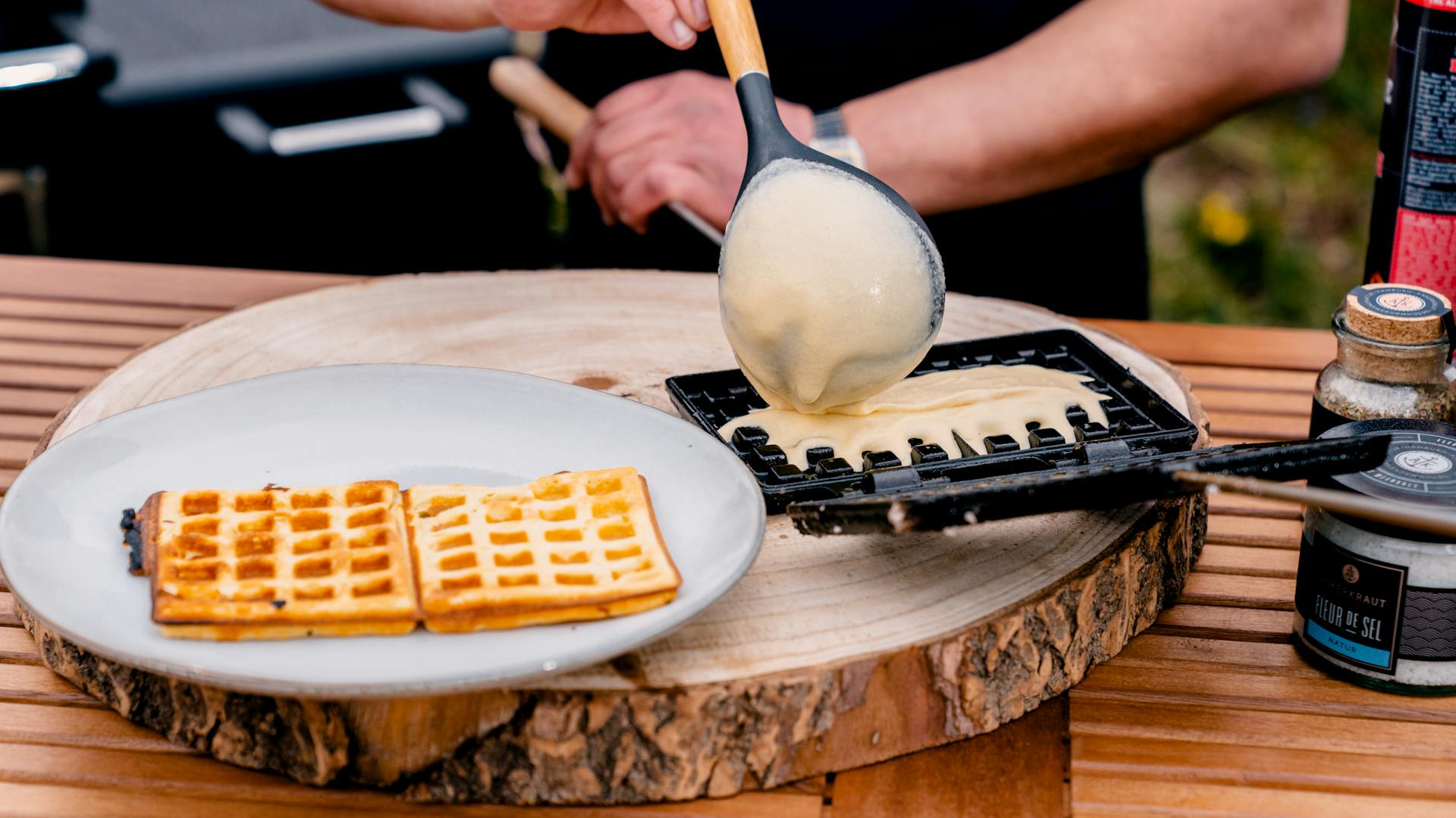 Kezek tésztát öntenek egy gofrisütőbe