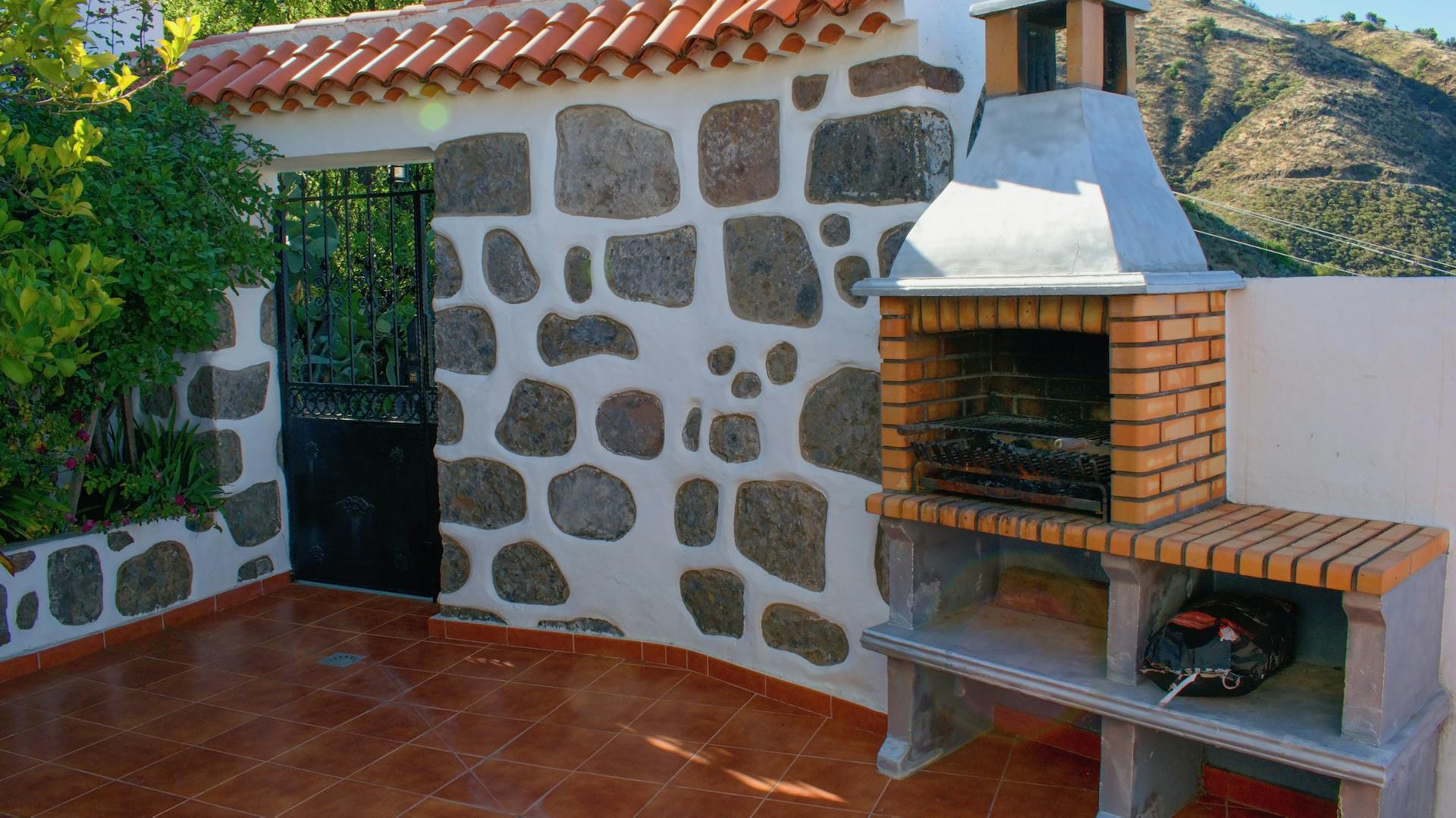 Murovaný gril z tehál vedľa kamennej steny v záhrade v stredomorskom štýle