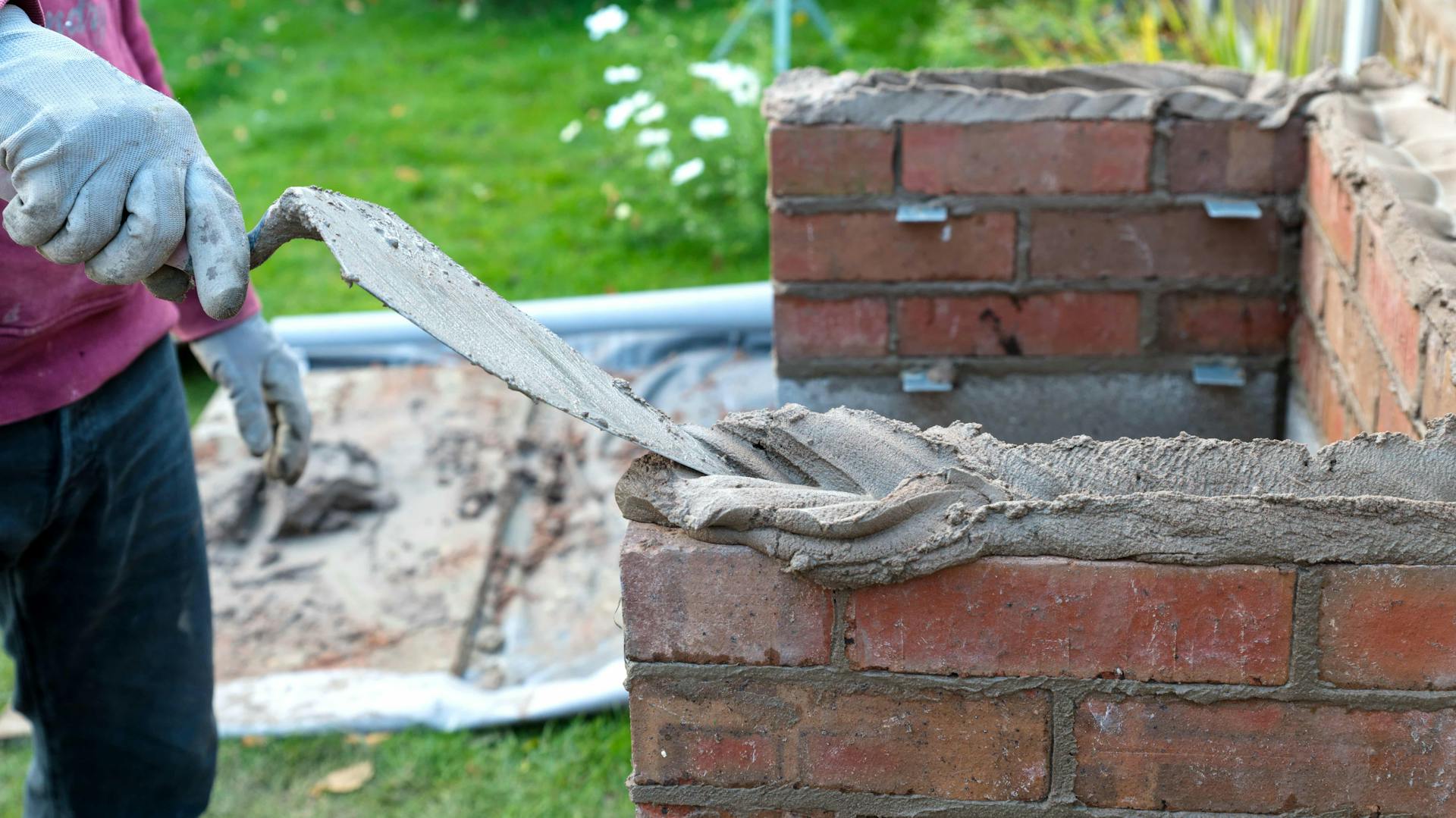 Jemand mauert einen Grill und gibt Mörtel auf Ziegelsteine.