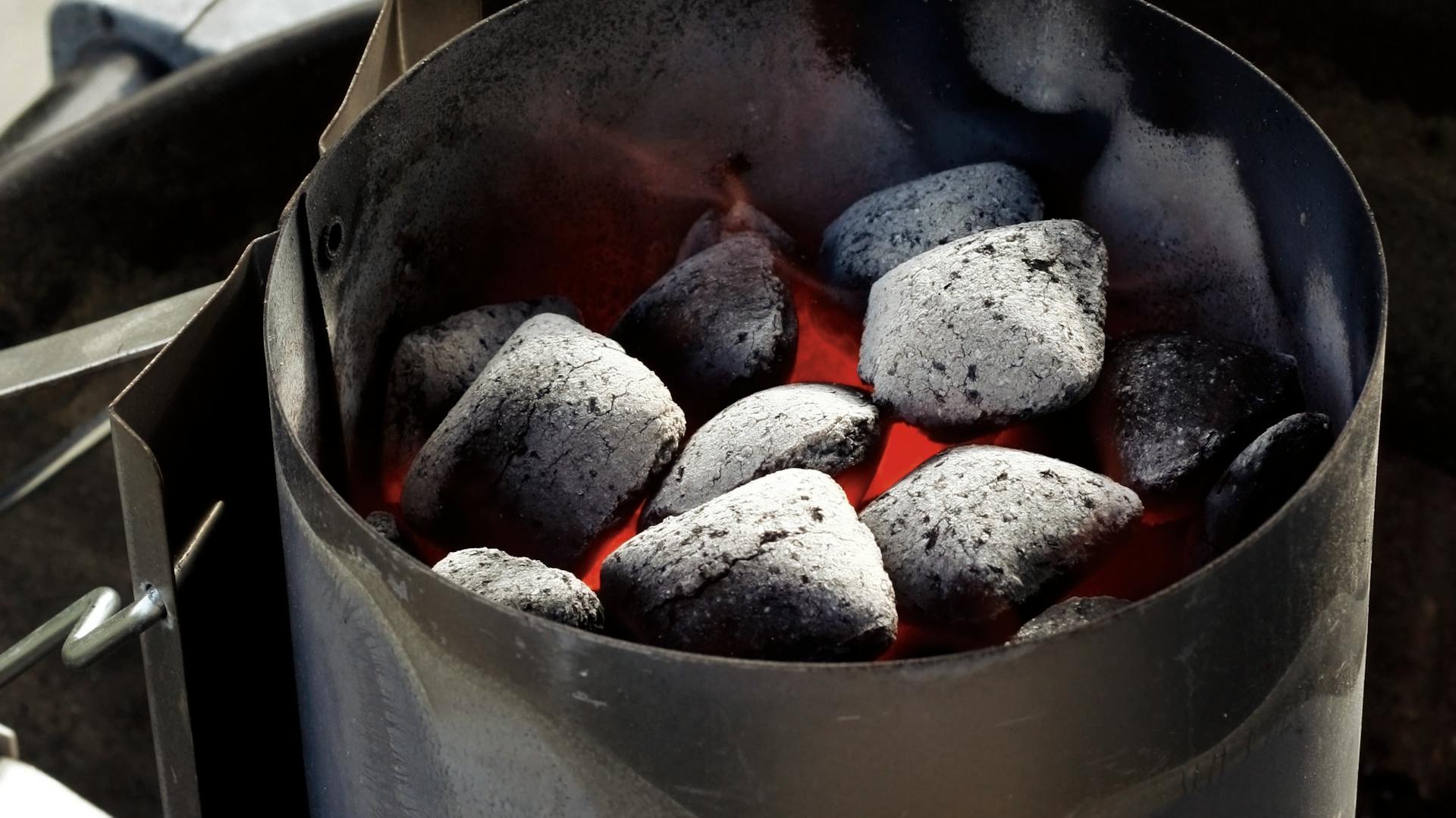 Holzkohle im Anzündkamin neben Grillzange