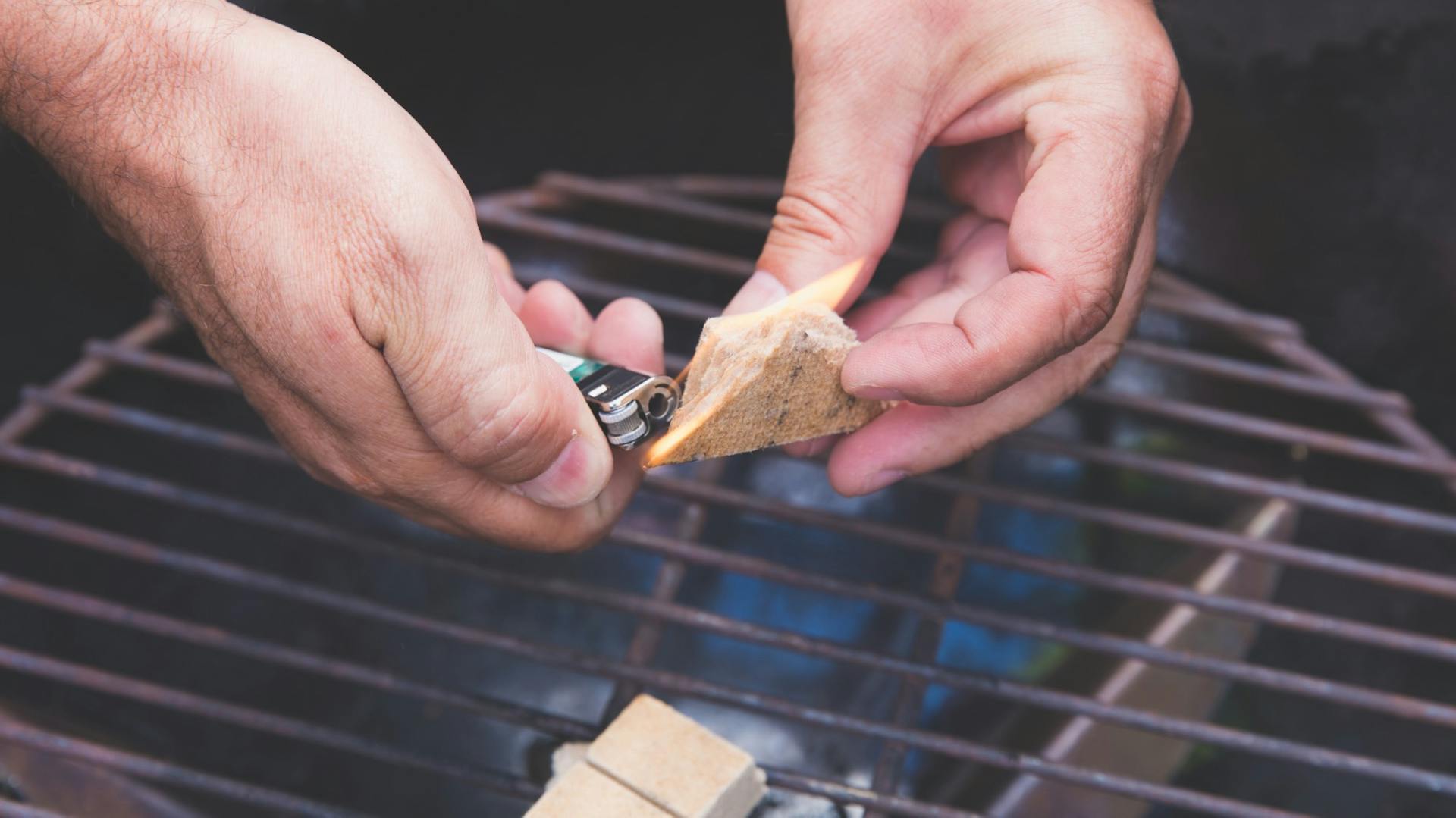 Hände feuern mit Grillanzündern und Streichholz einen Holzkohlegrill an