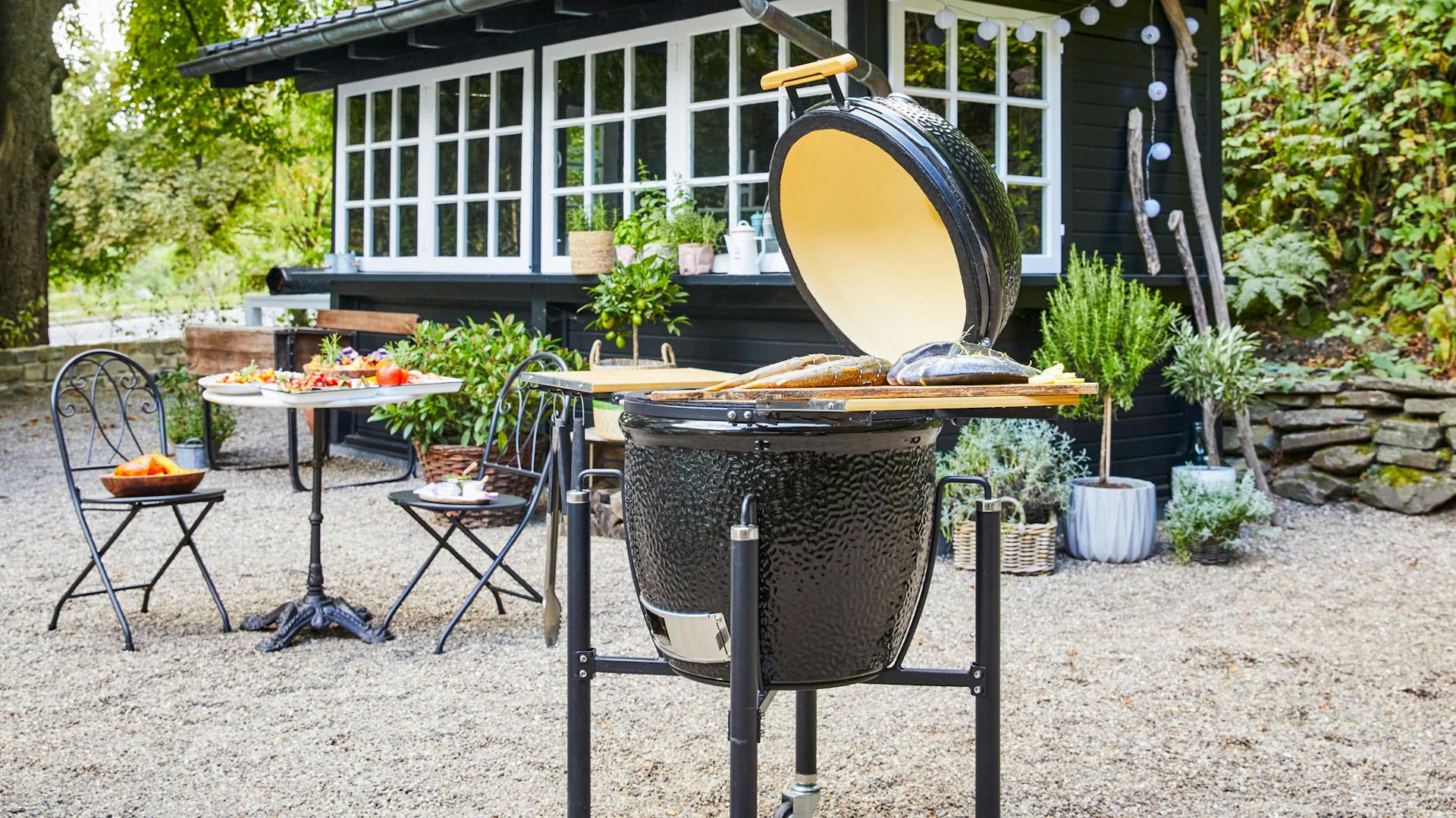Grillei steht vor Gartenhaus und gedecktem Tisch