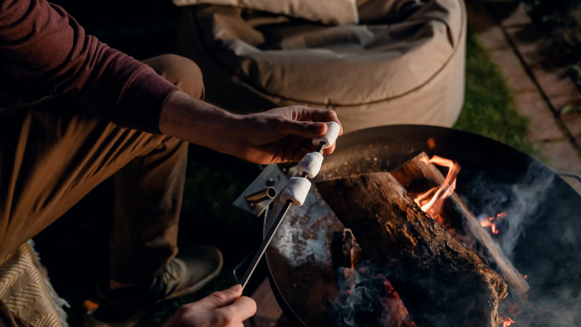 Person hält Stecken mit Marshmallows in Feuer in Feuerschale.