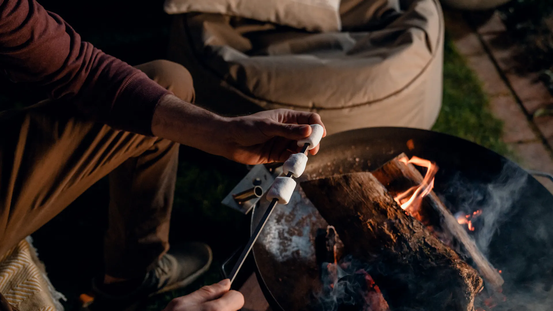 Person hält Stecken mit Marshmallows in Feuerschale