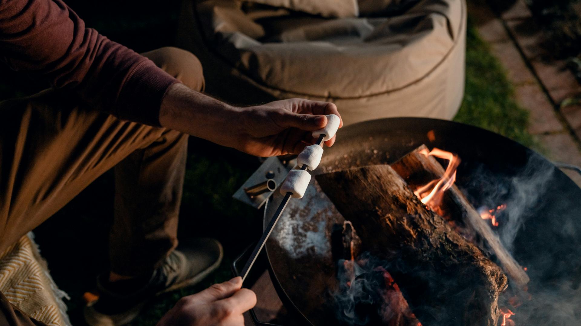 Person hält Stecken mit Marshmallows in Feuer in Feuerschale.