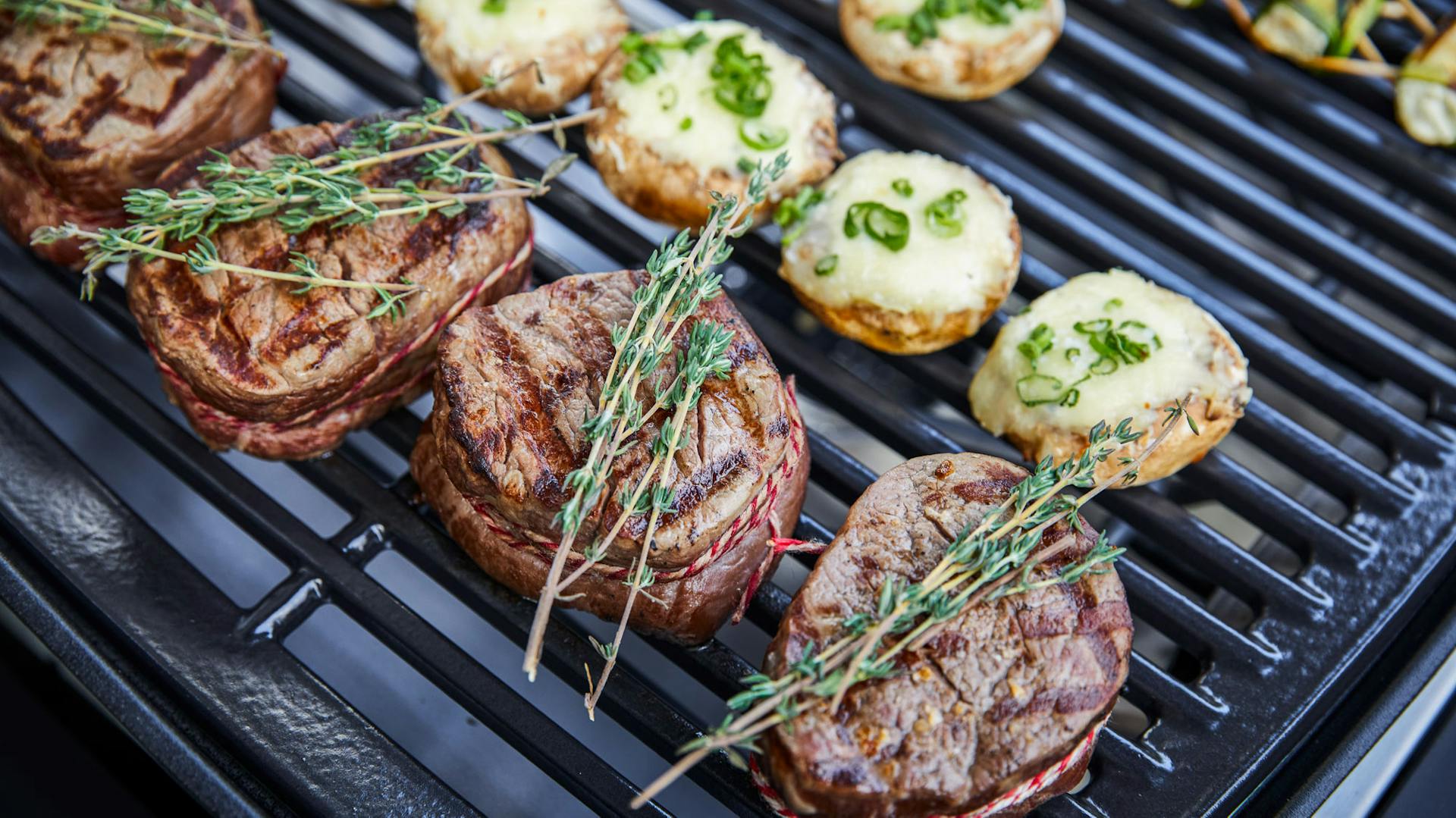 Gegrillte Steak mit Rosmarinzweigen neben gefüllten Champingnons.
