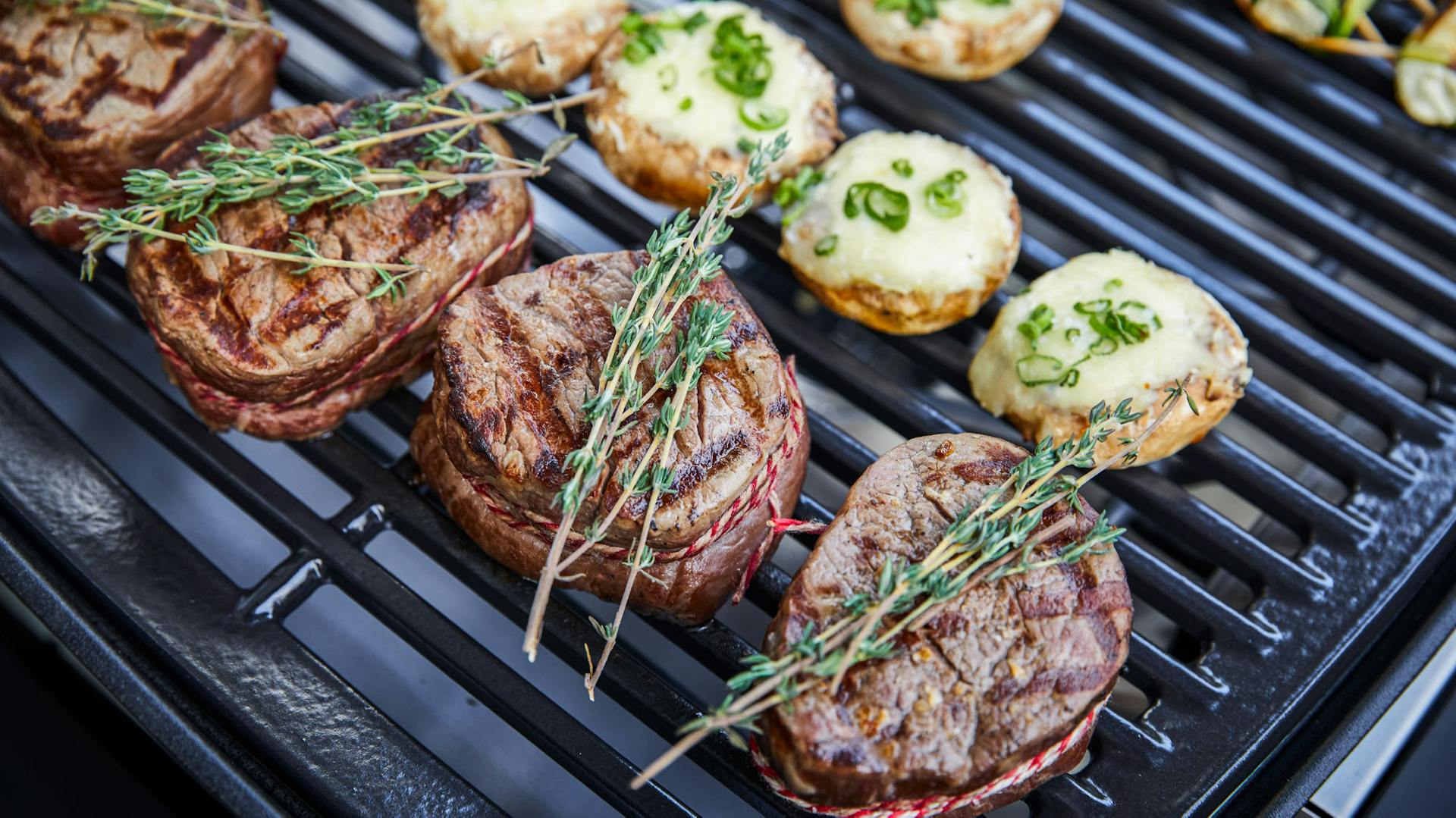 Gegrillte Steaks mit frischen Rosmarinzweigen neben gefüllten Champignons.