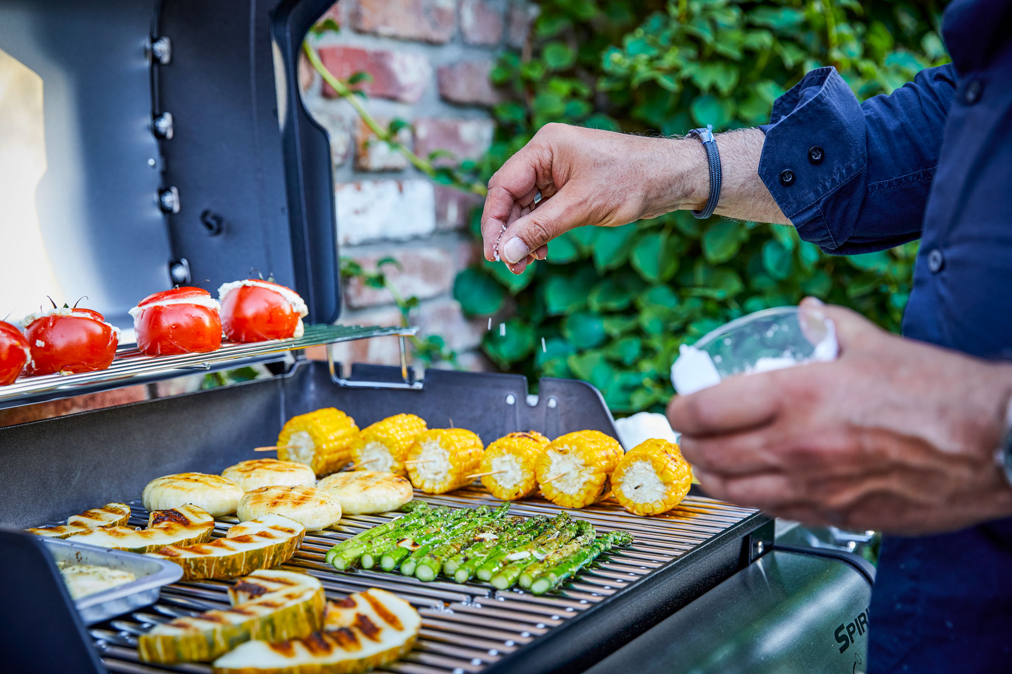 Mann würzt Gemüse auf Grill