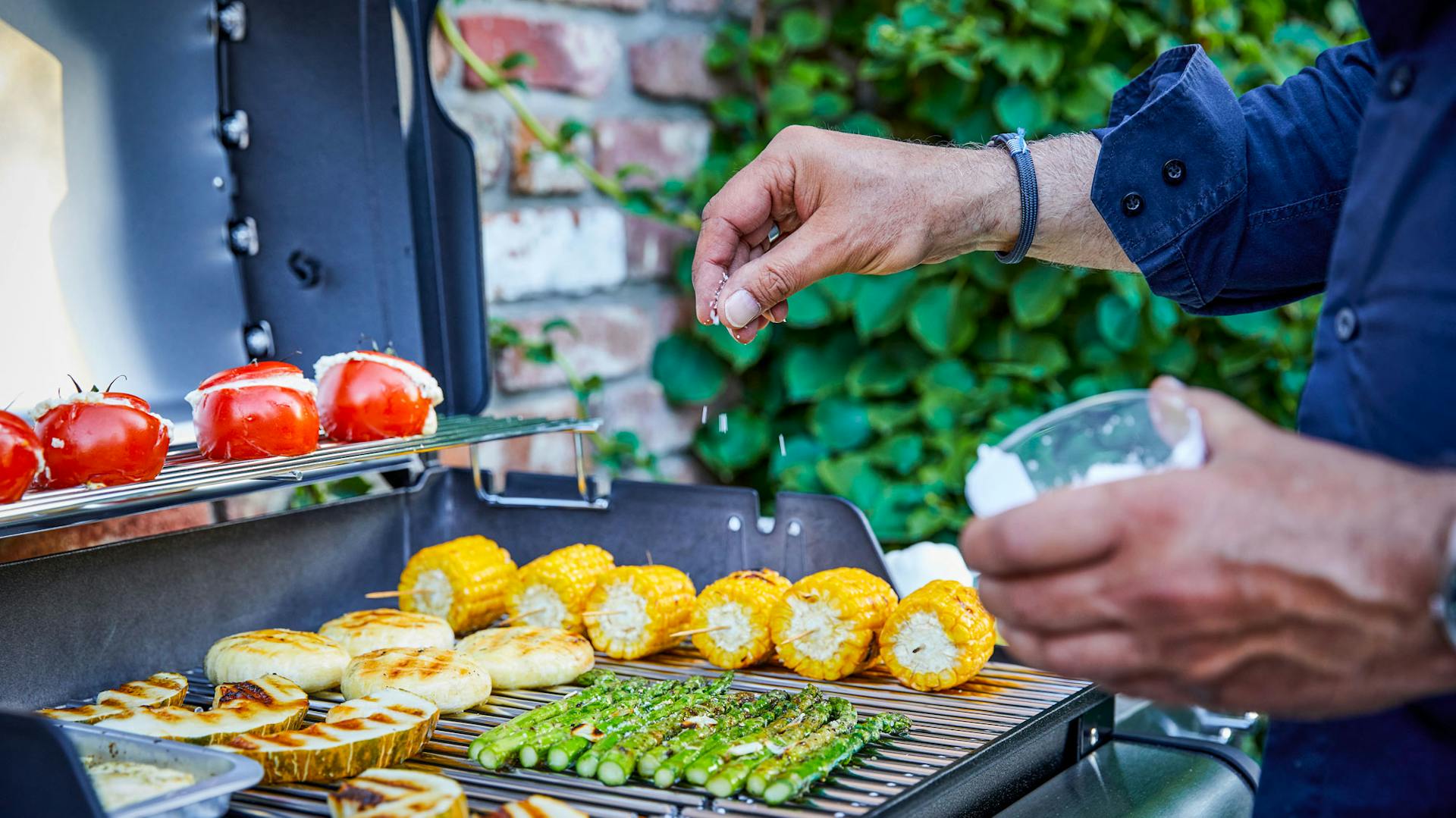 Mann würzt Gemüse auf Grill