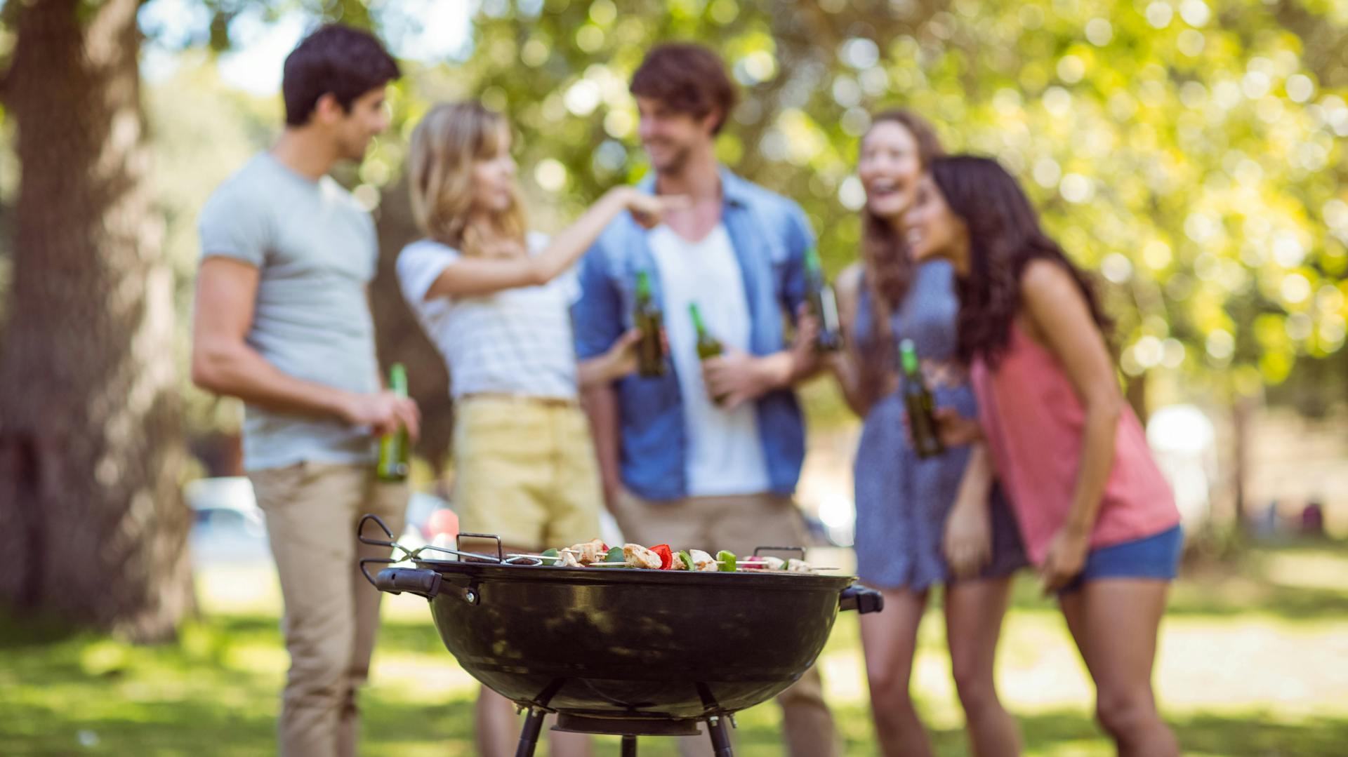 Mehrere Leute stehen vor einem Kugelgrill, auf dem Grillgut liegt.