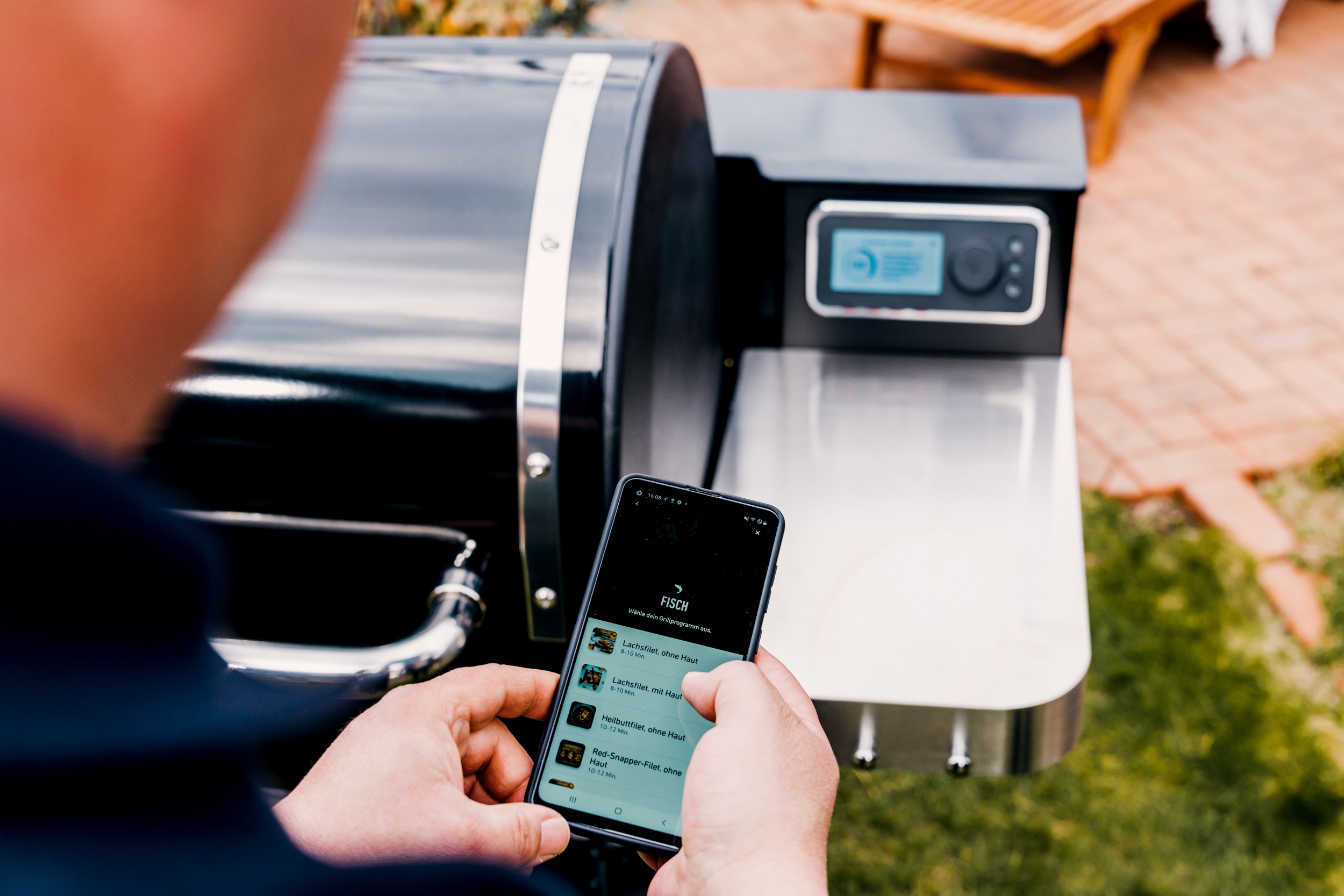 Mann hält Handy mit App zum smart Grillen.