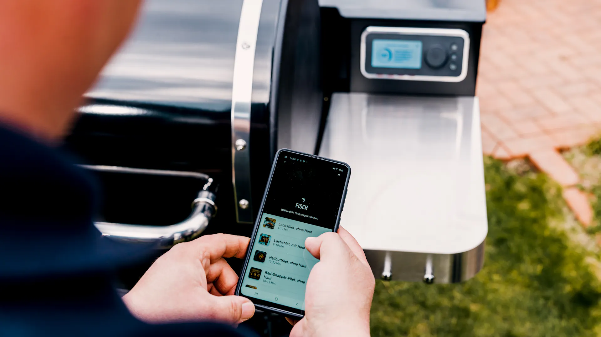 Mann hält Handy mit App zum smart Grillen.