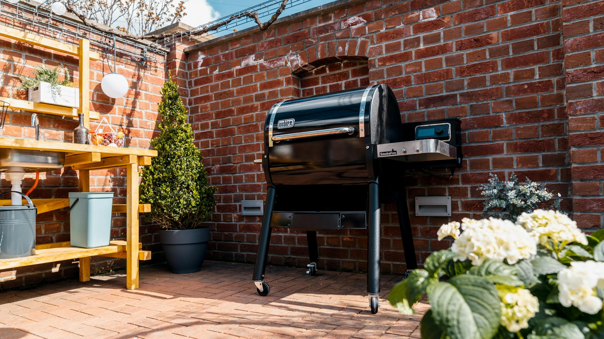 Grill steht an Gartenmauer neben Outdoorküche im Garten.