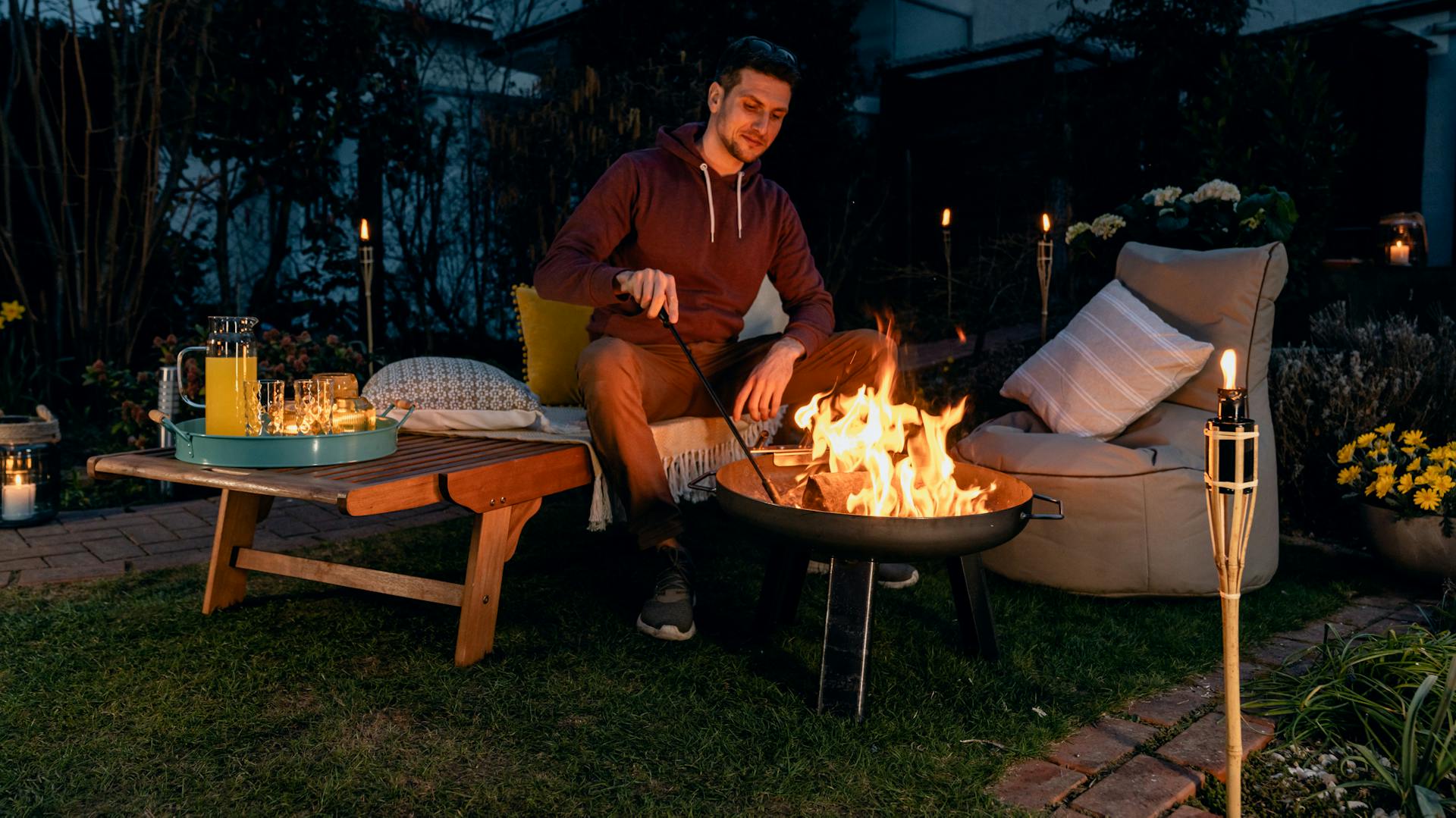 Person am Abend vor offenem Grill mit Sitzplatz