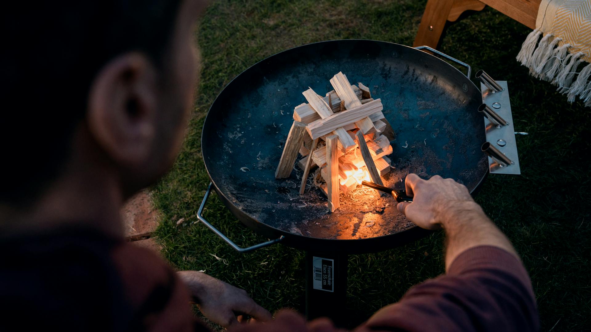 Una persona accende un fuoco nel braciere con legna accatastata e un accendino.