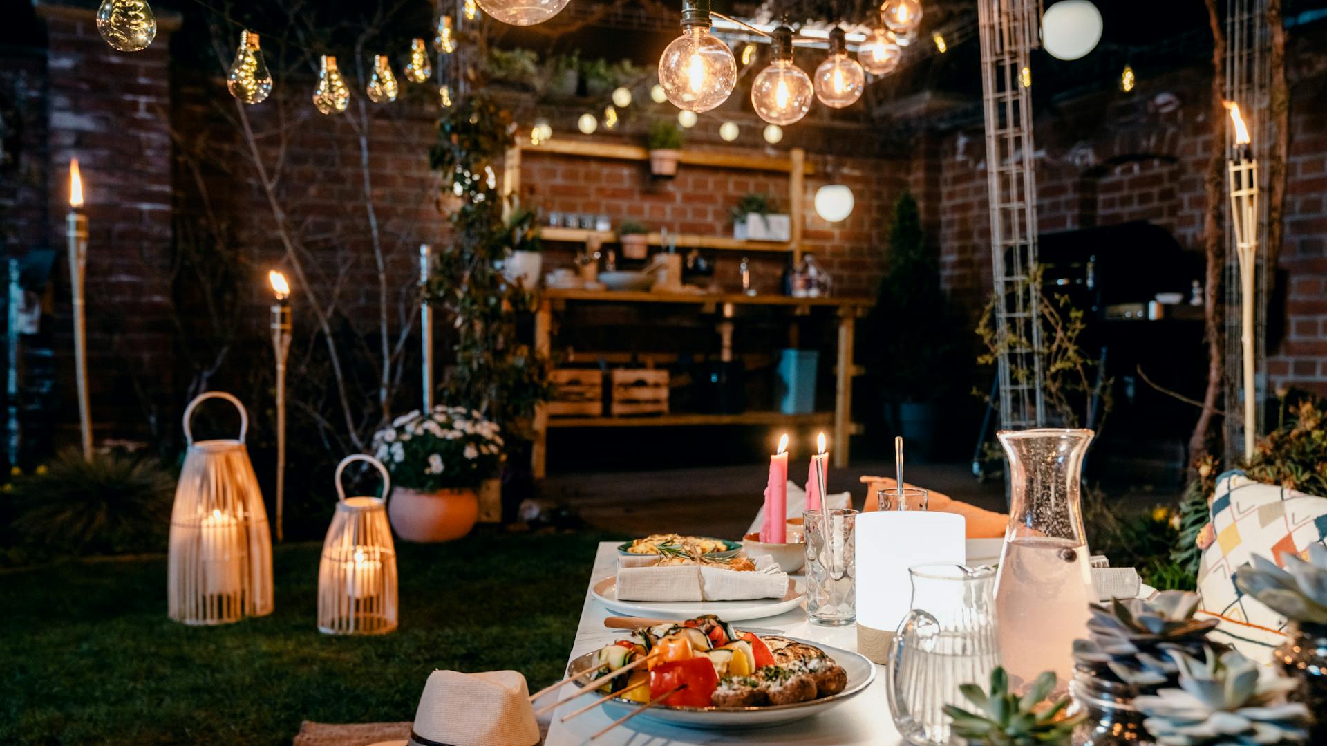 Grigliata in giardino illuminata da lanterne, ghirlande luminose, candele e lampade