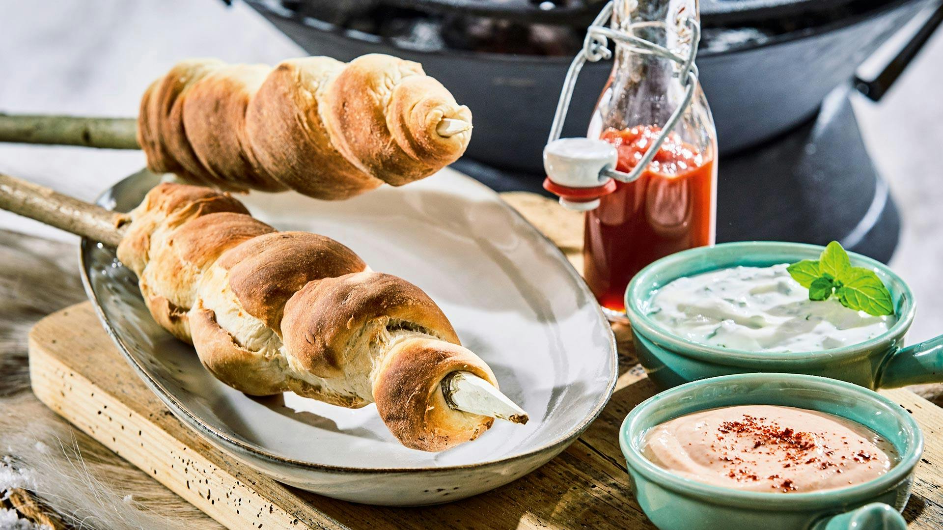 Gebräuntes Stockbrot auf Teller neben Dips
