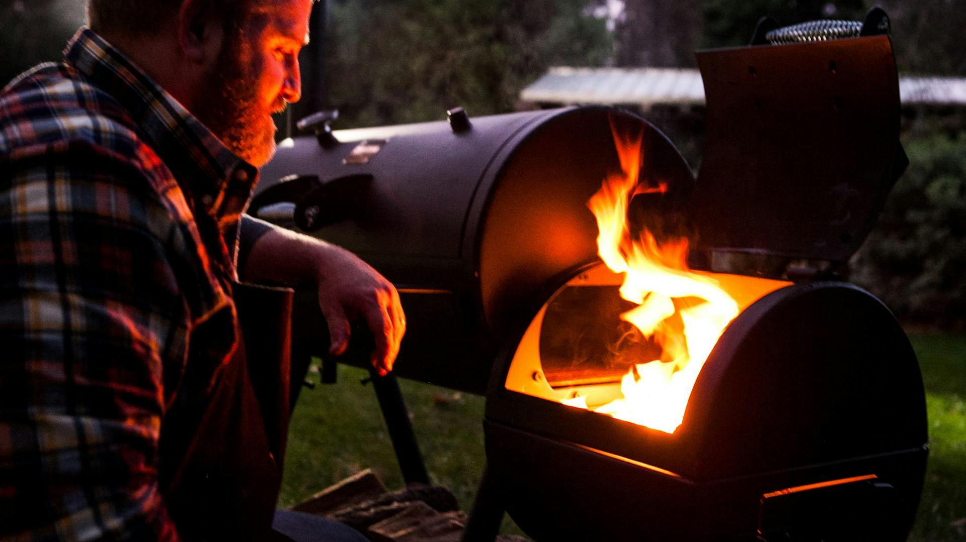 Mann steht vor der Brennkammer eines Smokers
