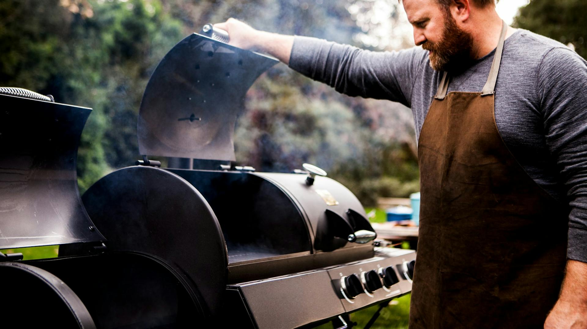 Mann mit Schürze öffnet Garraum von Smoker