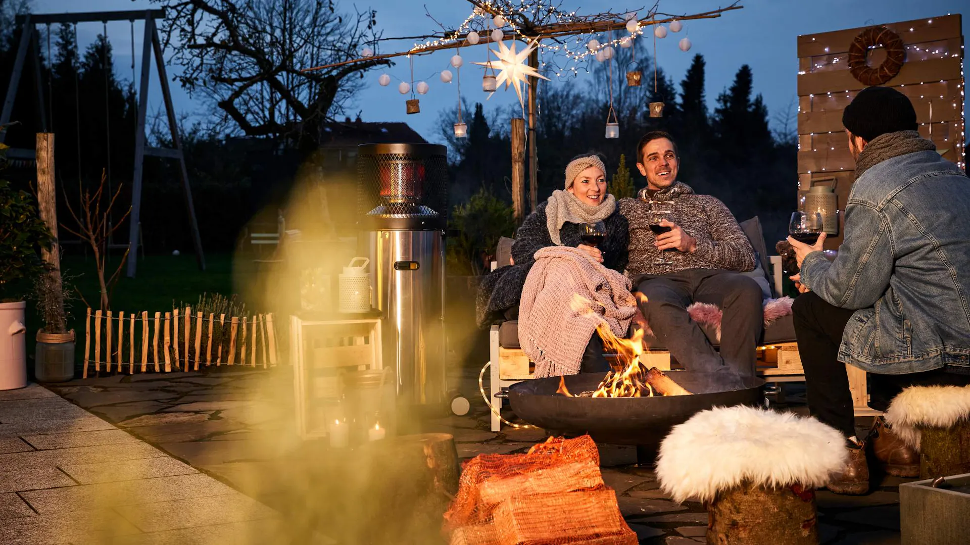 Personen sitzen abends um Feuerschale im Garten.