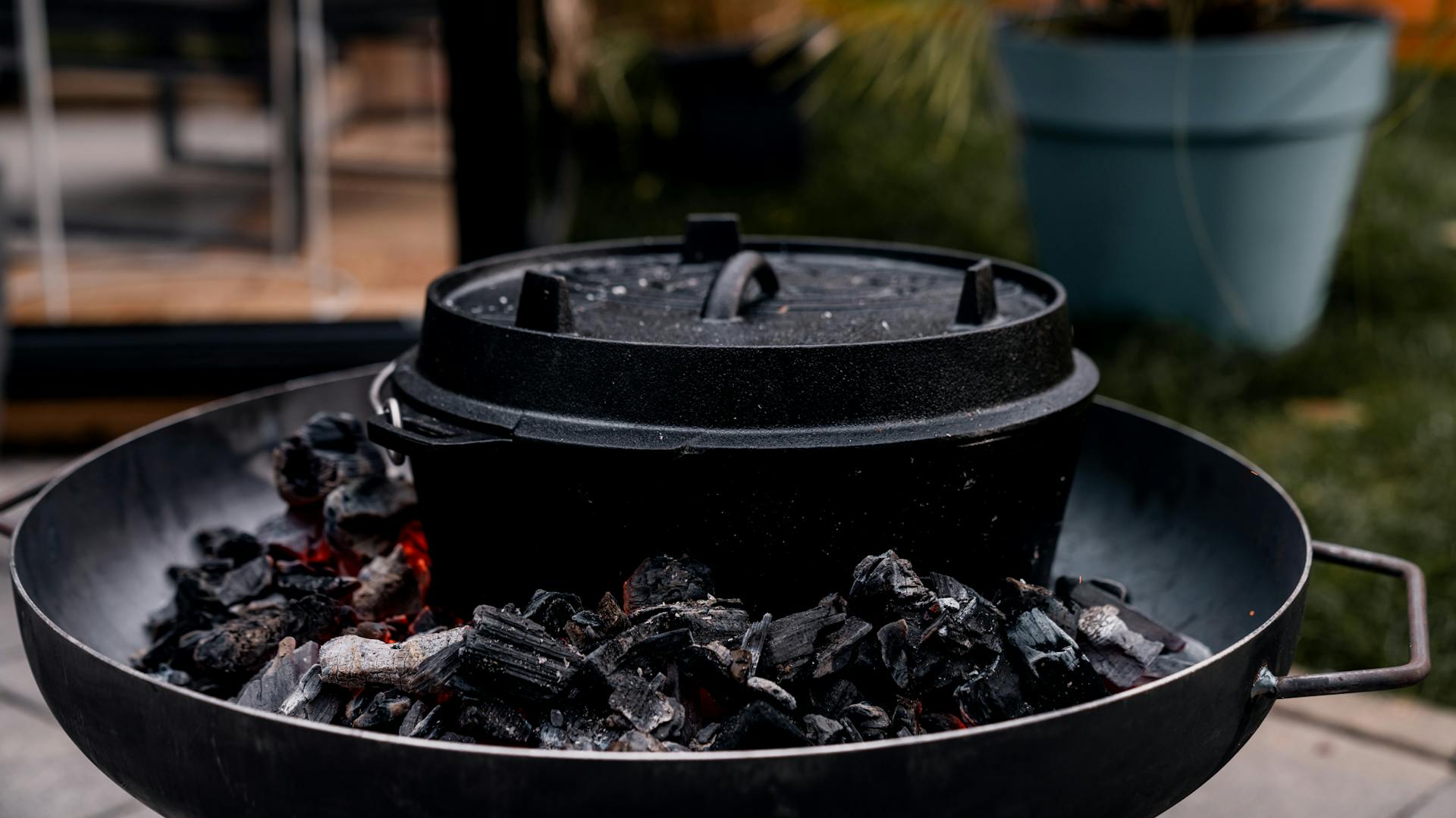 Ein gusseisener Topf steht geschlossen in der Mitte einer Feuerschale. Die Kohlen um ihn herum glimmen schwach.