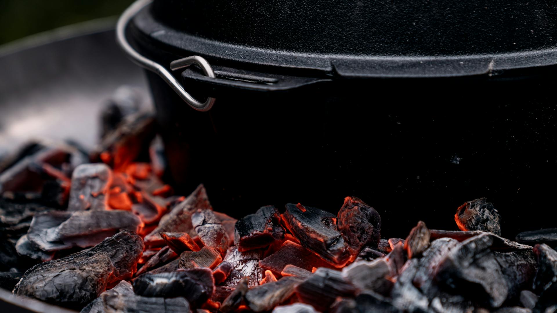 Untere Kanten eines gusseisernen Topfs inmitten von glühenden Kohlen.