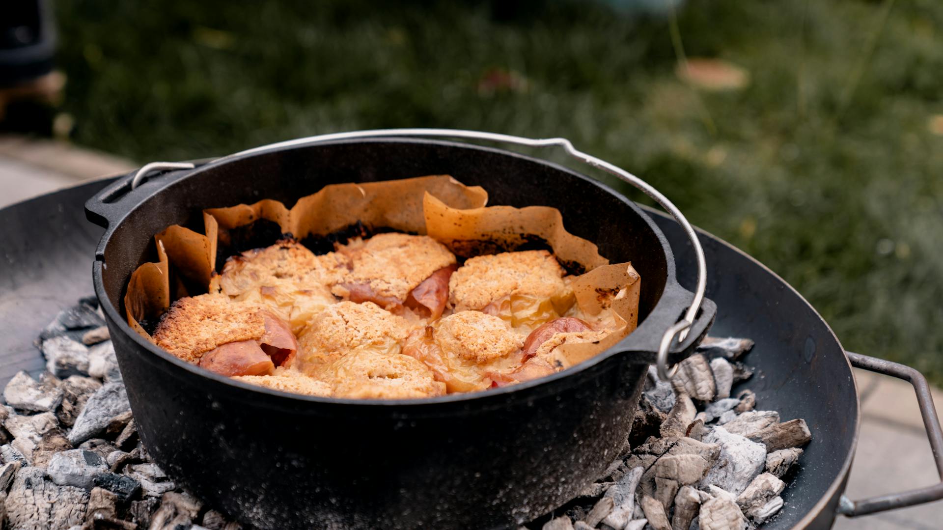 Offener Dutch Oven auf glühenden Kohlen, voll mit dampfenden Bratäpfeln.