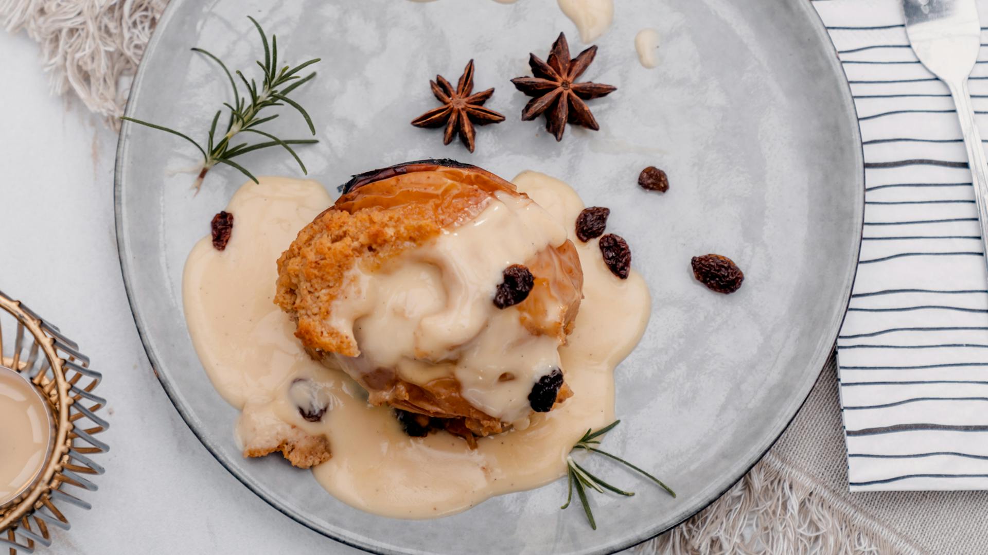 Draufsicht auf einen hellblauen Teller, auf dem ein angerichteter nBratapfel mit Vanillesoße und Gewürzen liegt.