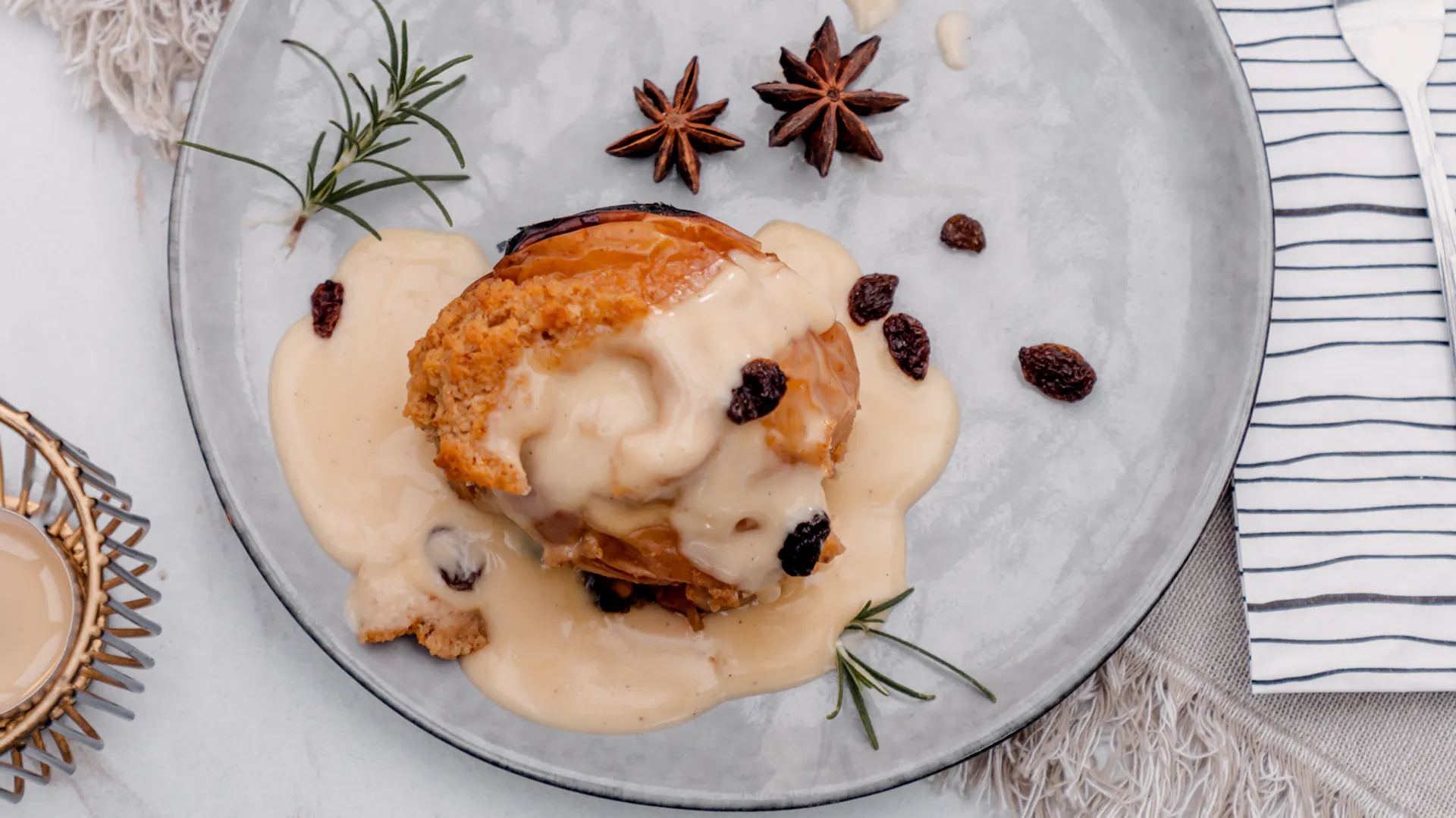 Világoskék tányéron sült alma vaníliaszósszal, dióval és csillagánizzsal. Az asztal meleg, világos, természetes tónusokban pompázik.