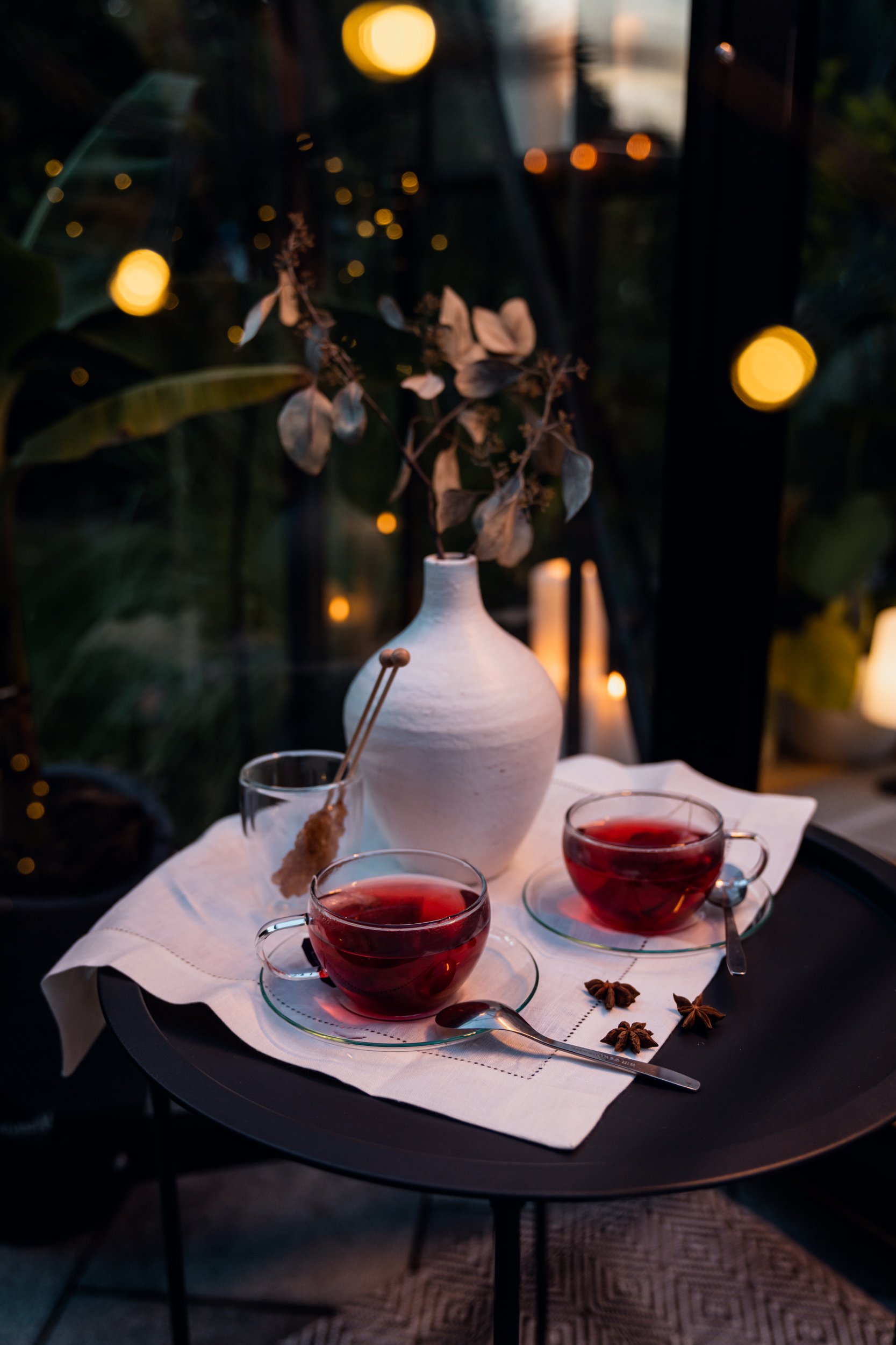 Zwei stimmungsvoll beleuchtete Tassen Tee stehen neben einer Vase vor dunklem Hintergrund.
