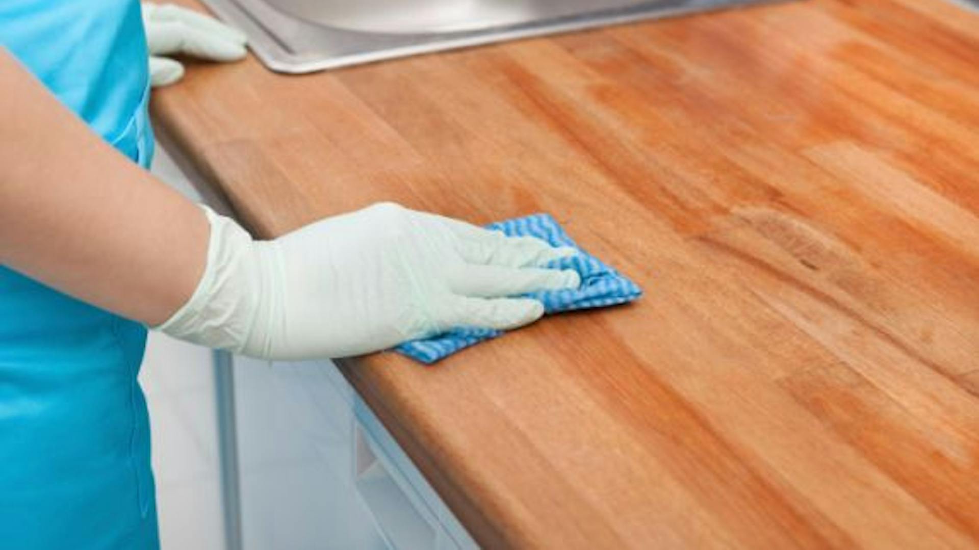 Person mit Handschuhen reinigt eine Küchenarbeitsplatte mit einen blauen Schwammtuch