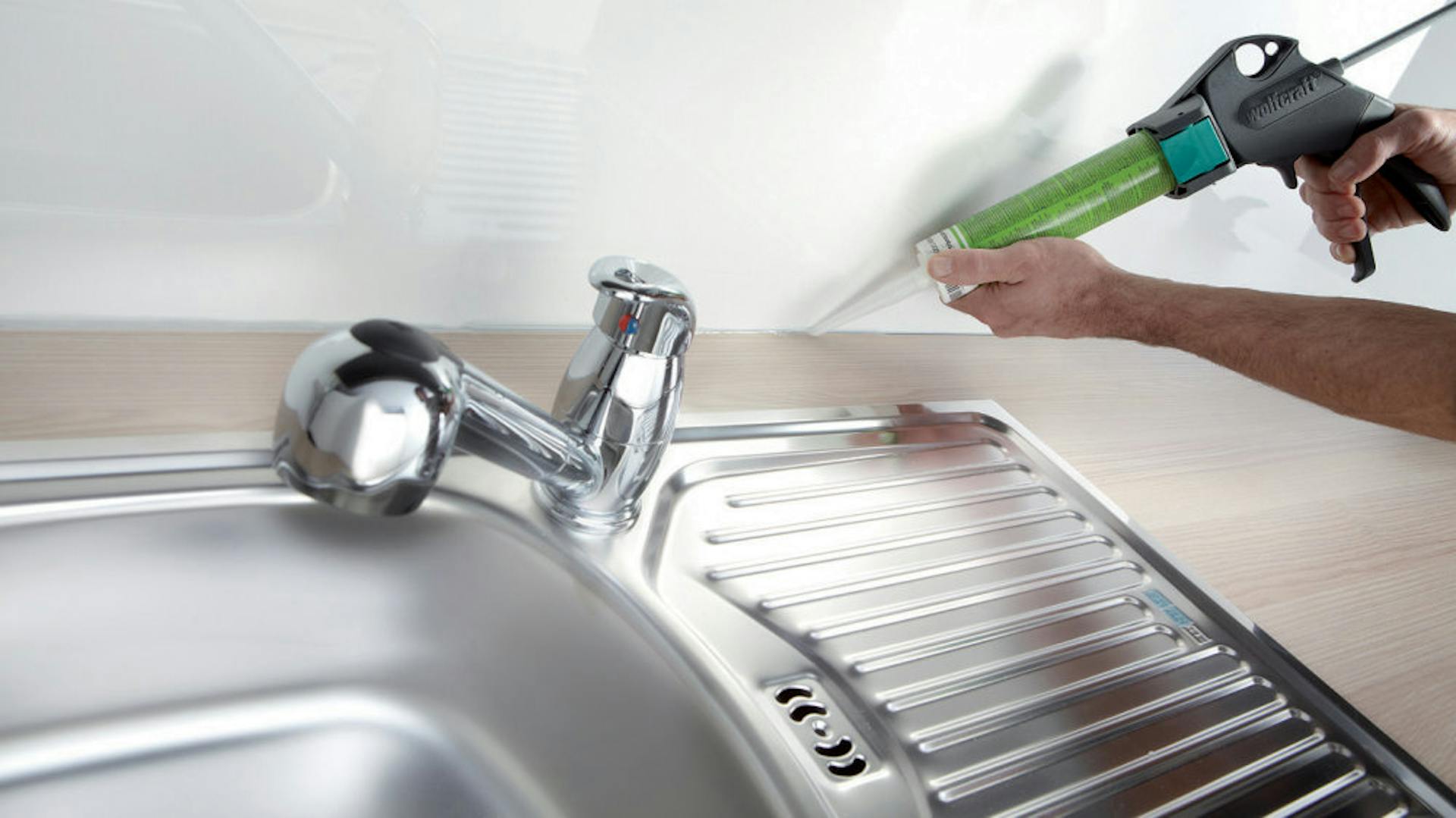 Heimwerker dichtet Arbeitsplatte zur Wand hin mit Silikon und Kartuschenpresse ab.