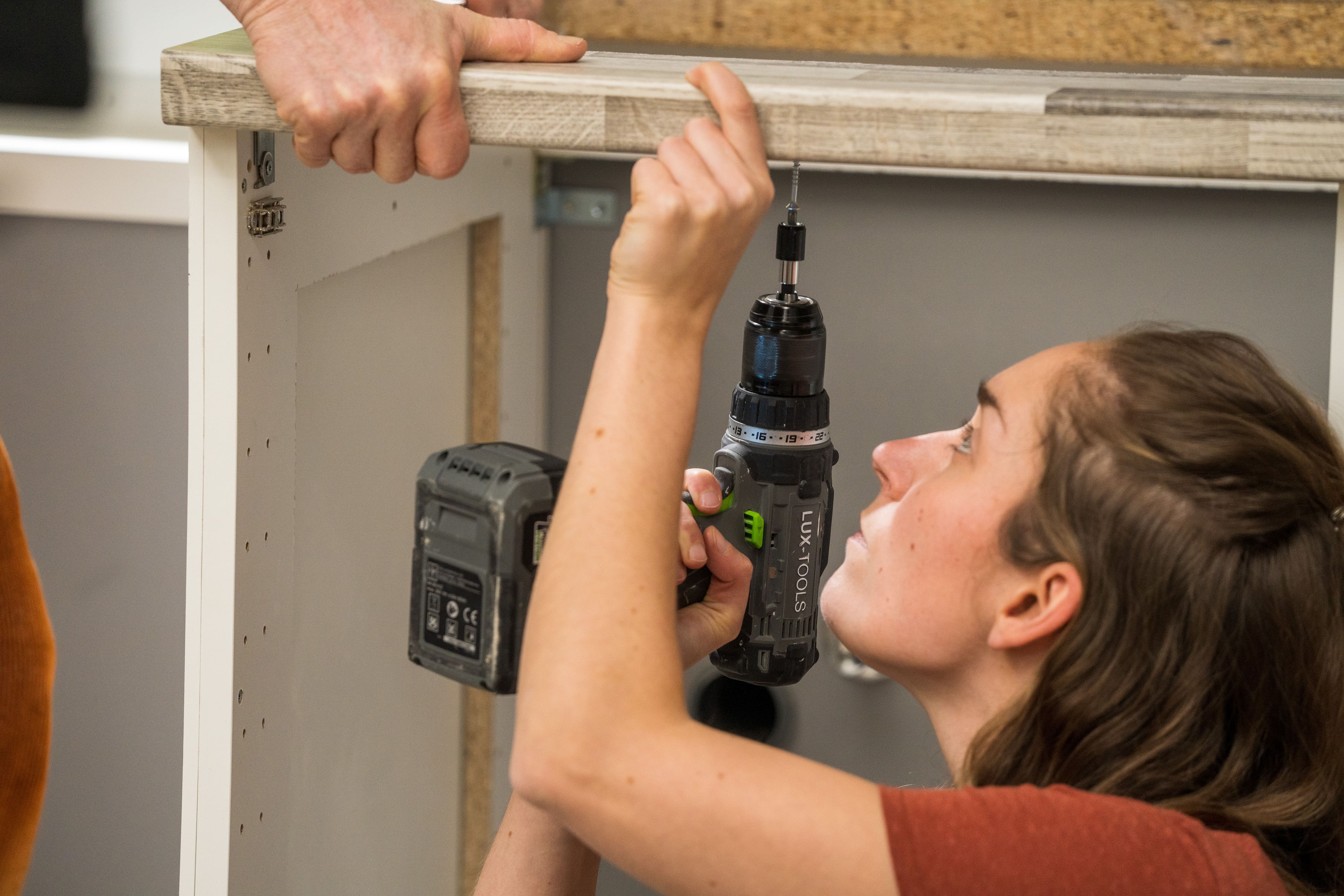 Domáci majster skrutkuje pracovnú dosku na spodné skrinky.