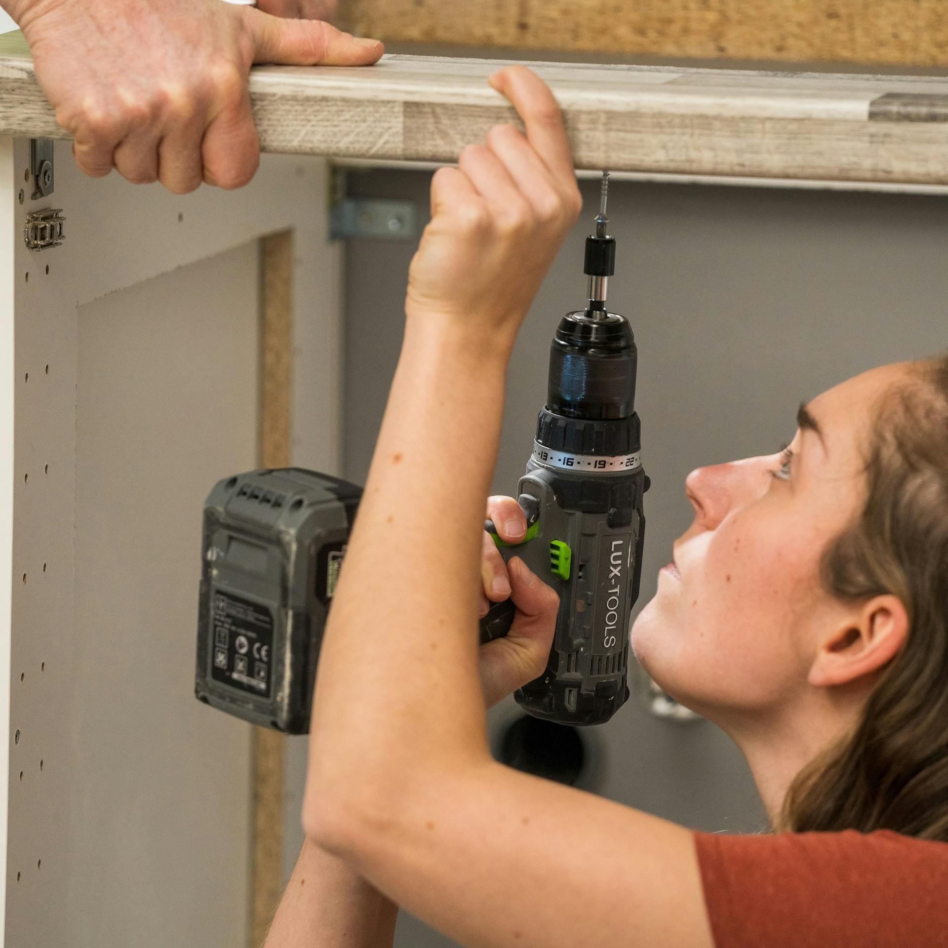 Domáci majster skrutkuje pracovnú dosku na spodné skrinky.