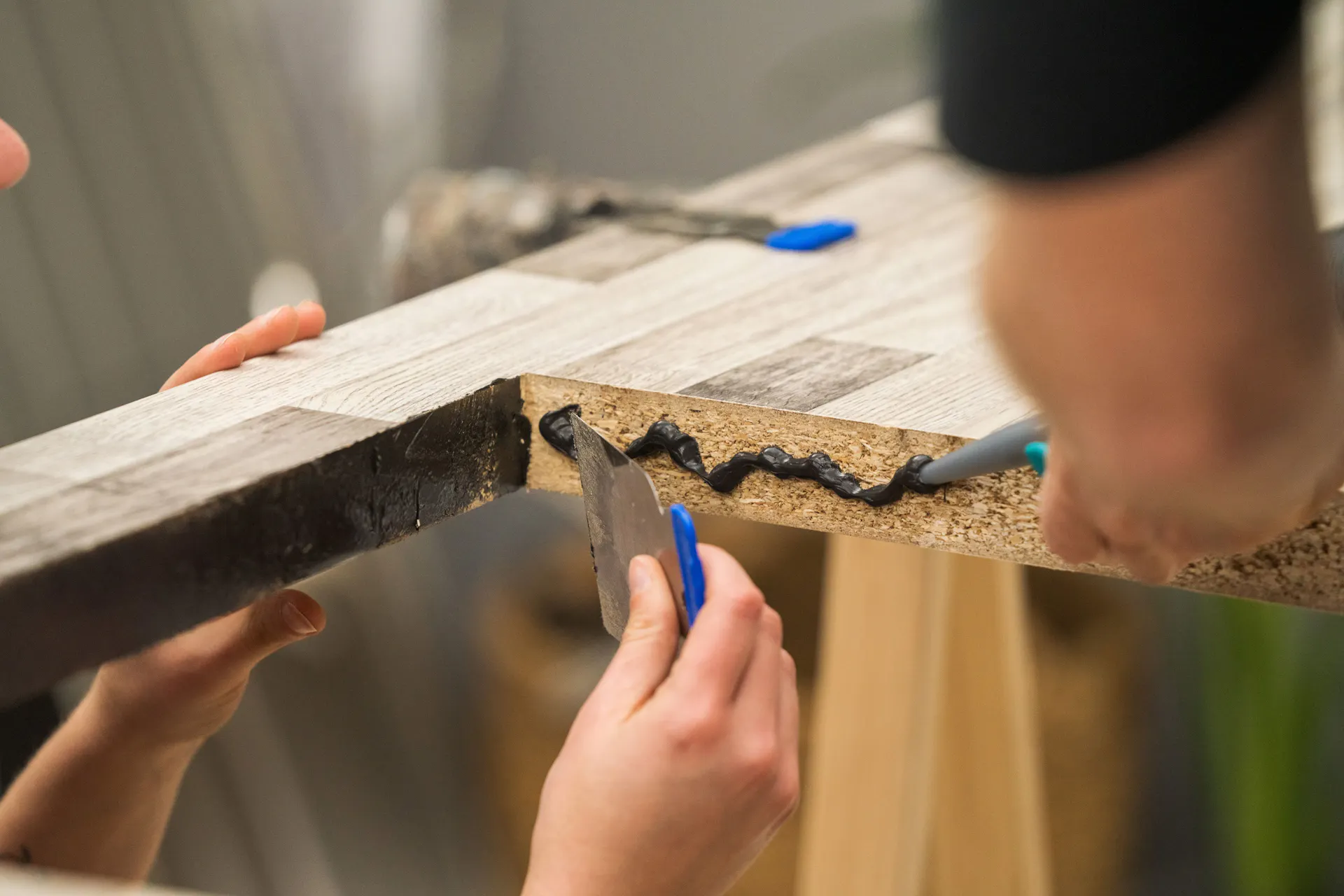 Egy barkácsoló szilikonnal és spatulyával szigeteli a vágott éleket.