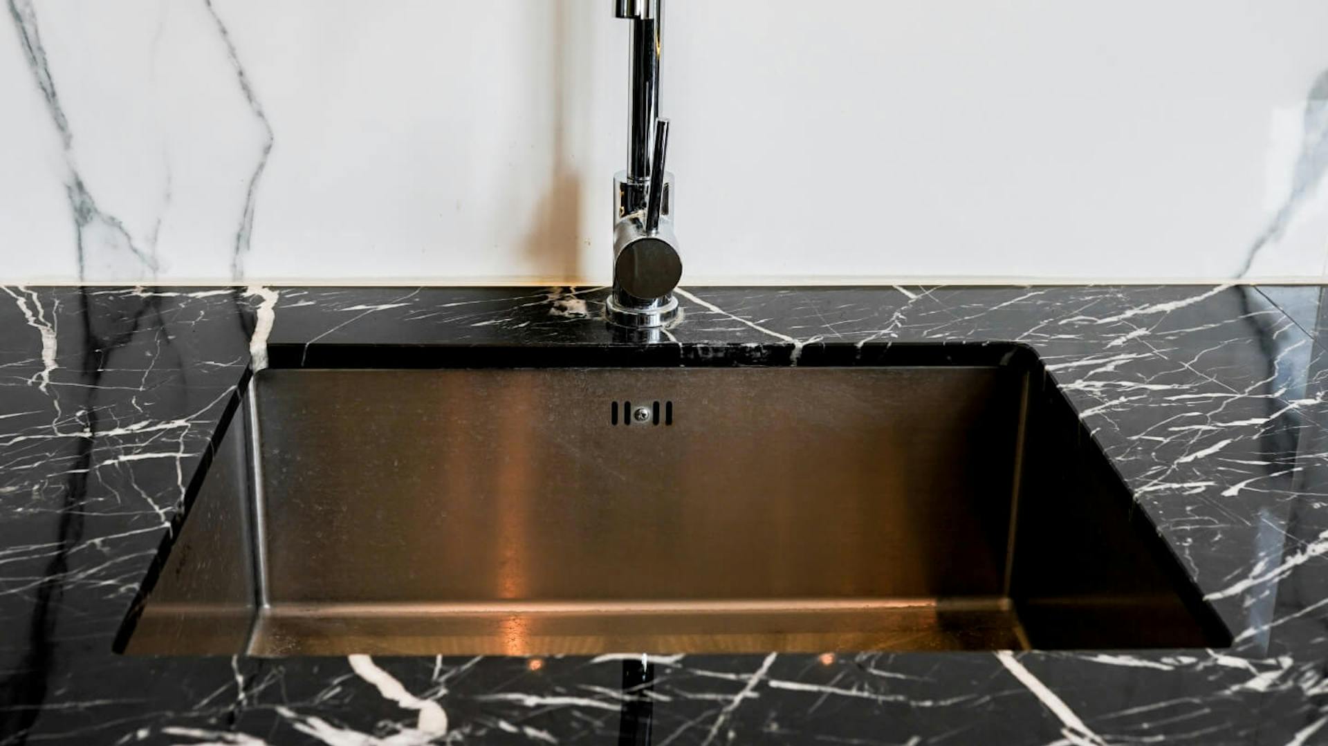 Sötét márványhatású konyhai munkalap, világos márványhatású konyhai hátfal. Sötét mosogatókagyló a munkalapba beépítve.