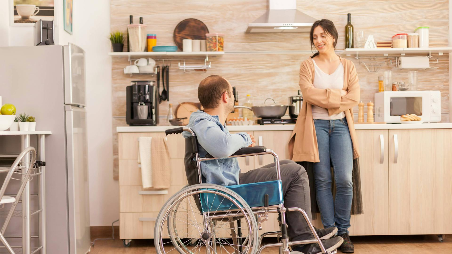 Ein Mann im Rollstuhl und eine Frau unterhalten sich in einer gewöhnlichen Küche.