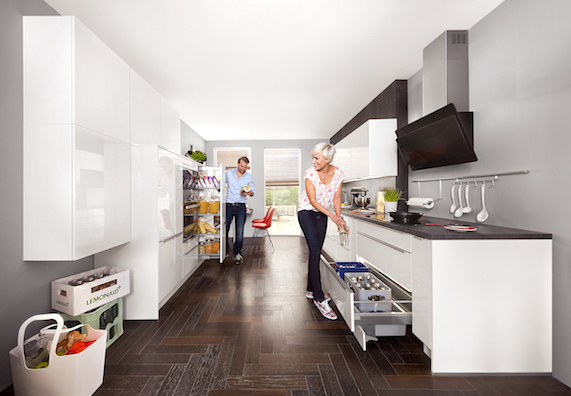Emberek tiszta konyhában, fehér konyhaszekrény a sötét padlón.