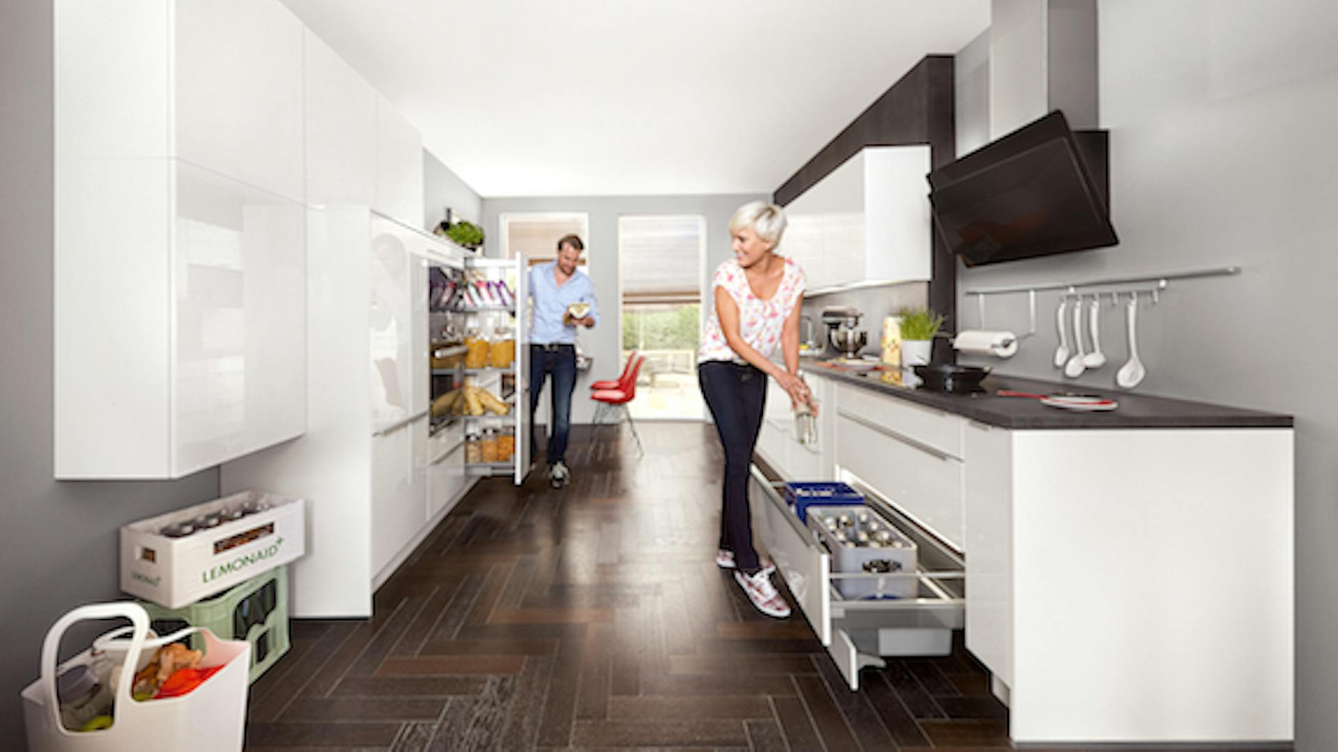 Emberek tiszta konyhában, fehér konyhaszekrény a sötét padlón.