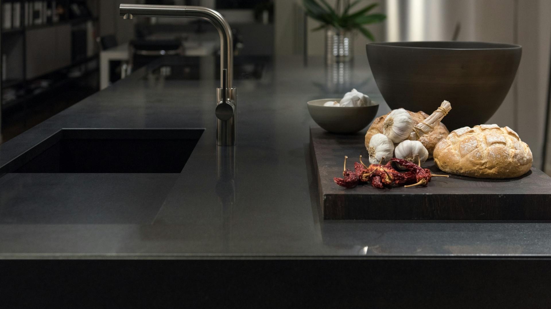 Schwarze Küche mit schwarzer Granitarbeitsplatte. Auf der Arbeitsplatte steht ein Brett mit Brot und Knoblauch.