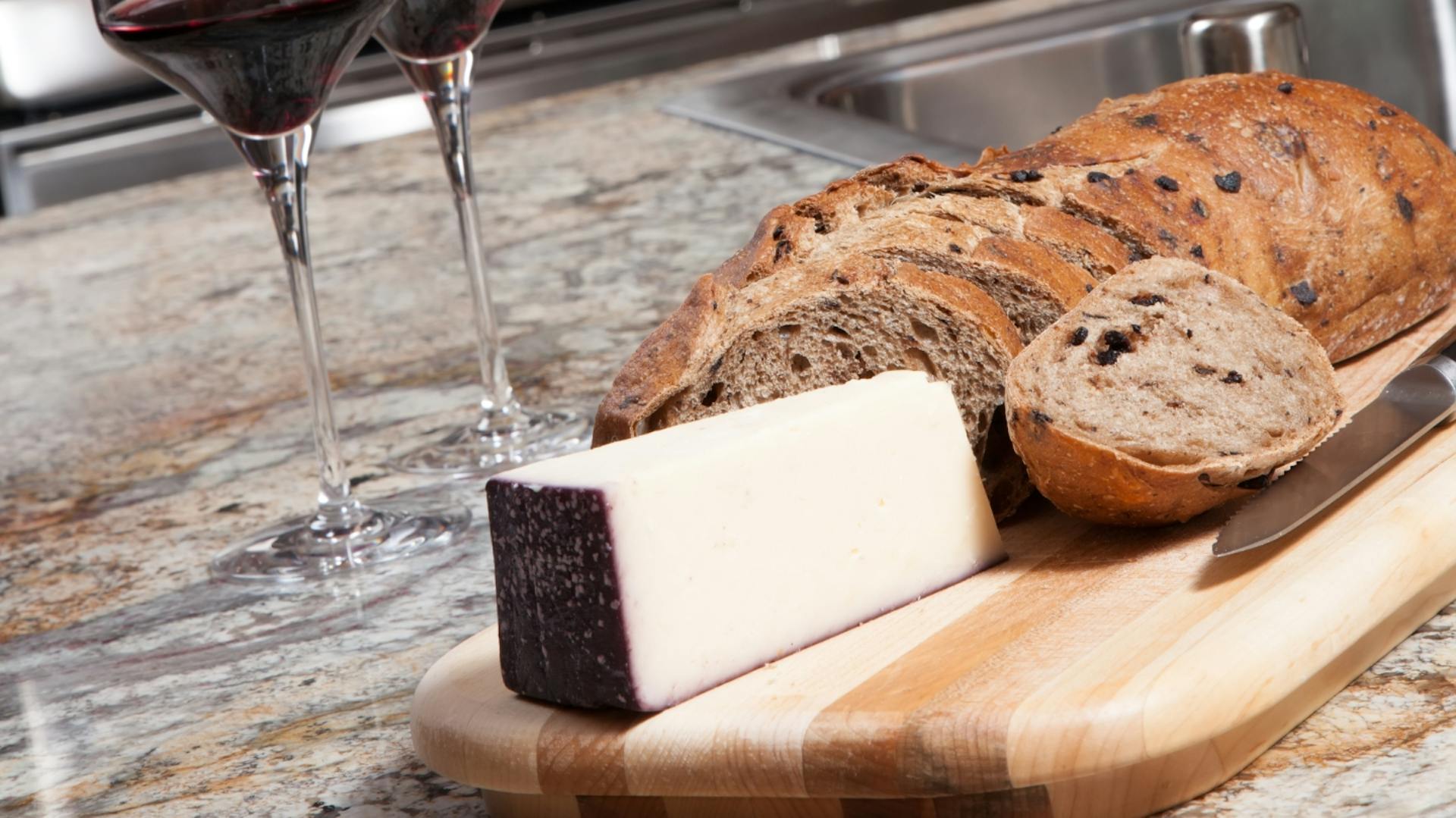 Zwei Gläser Wein, Käse und Brot stehen auf Granitarbeitsplatte.