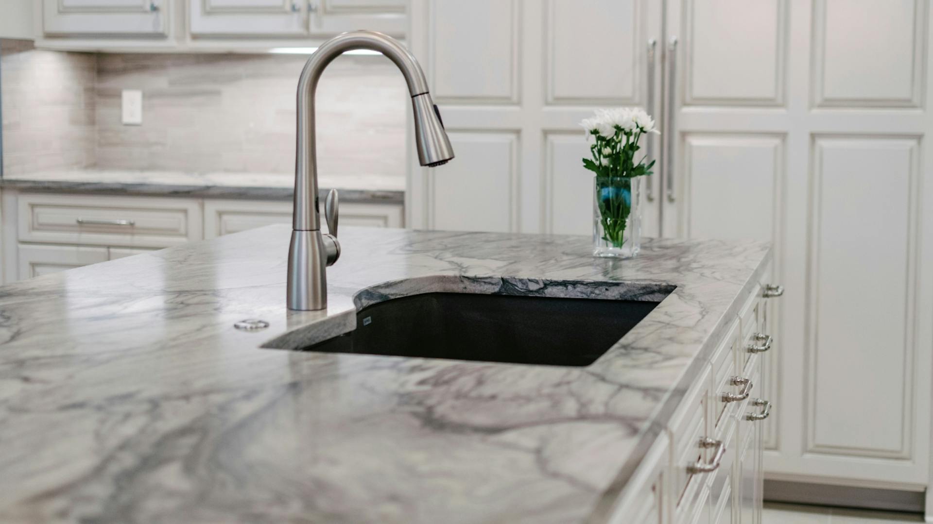 Helle Granitarbeitsplatte in der Küche mit eingelassenem Waschbecken und silbernem Wasserhahn.