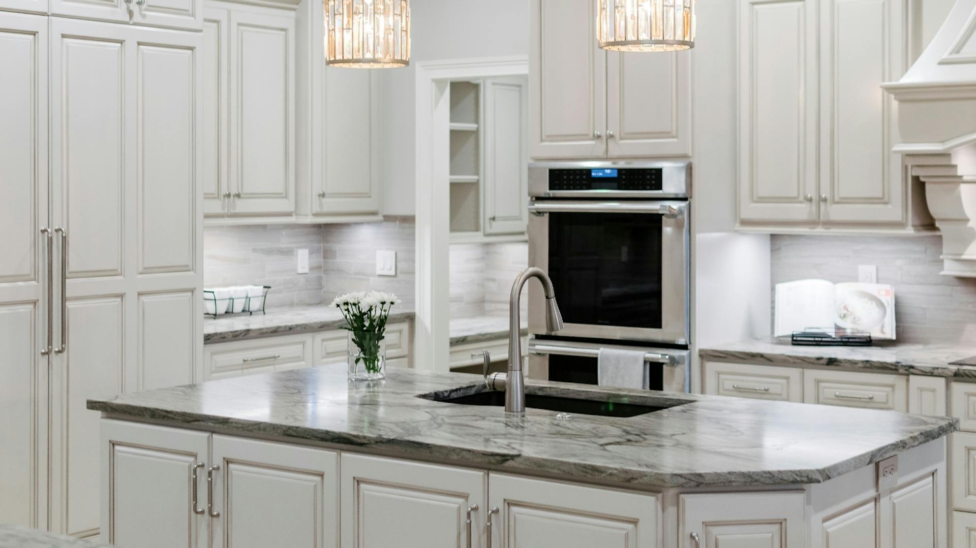 Weiße Küche mit Kochinsel. Arbeitsplatte aus grauem Granit. In der Kochinsel ist ein Waschbecken eingelassen.