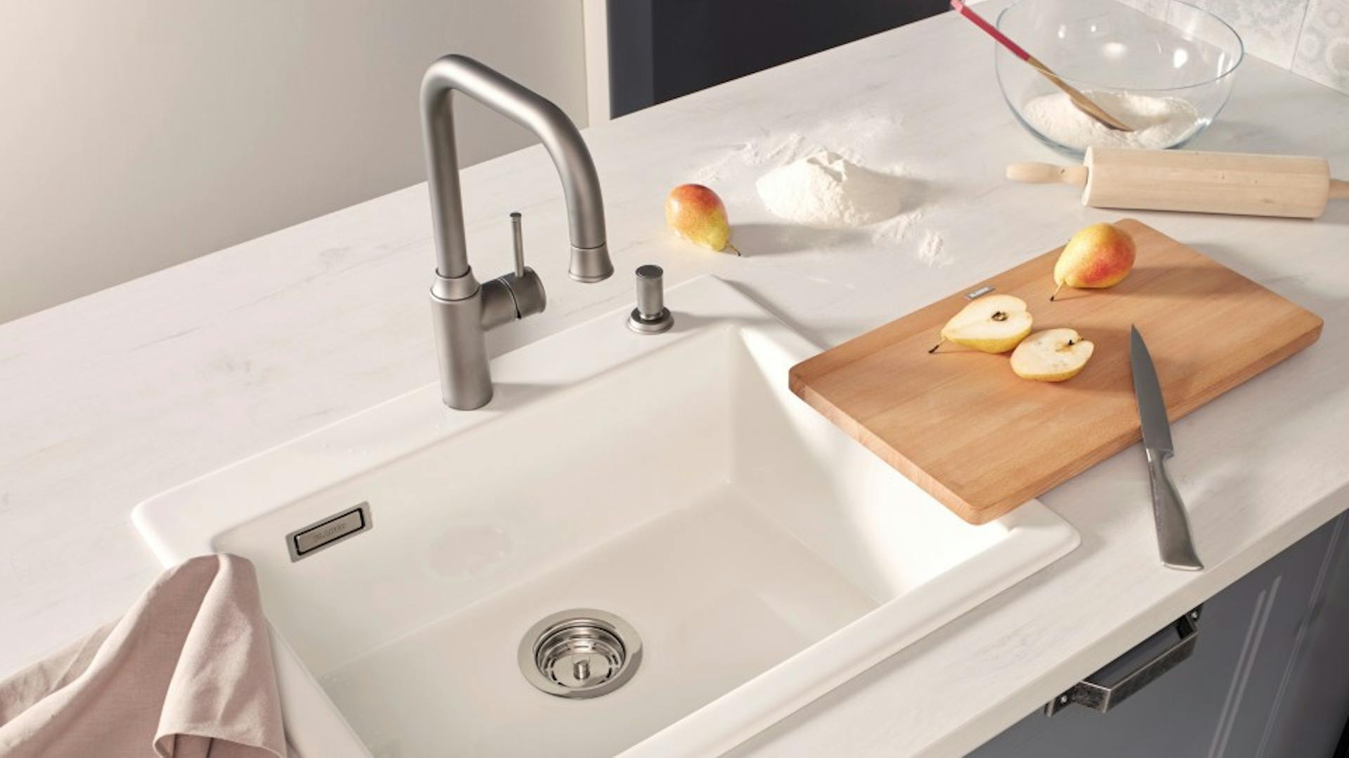 Világos kerámia mosogató vágódeszkával és konyharuhával
