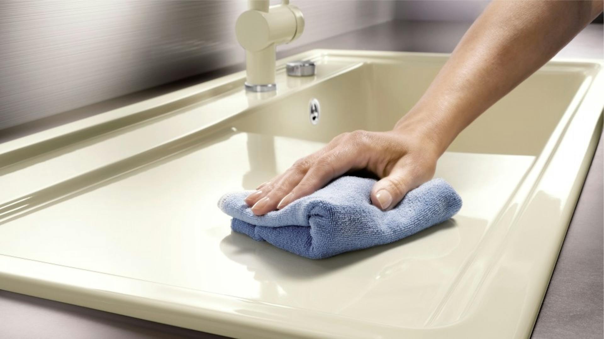 Person wischt eine Keramikspüle ab.