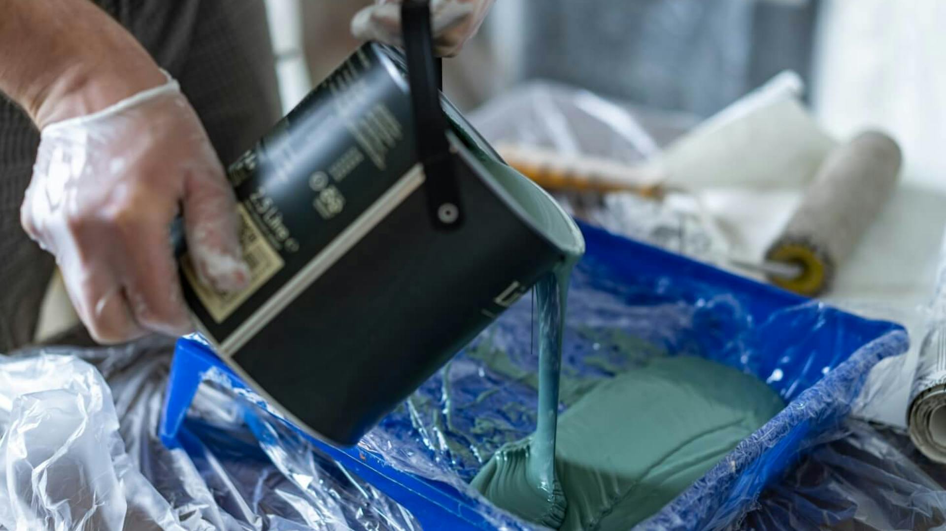 Jemand gießt Farbe in eine Farbwanne um.