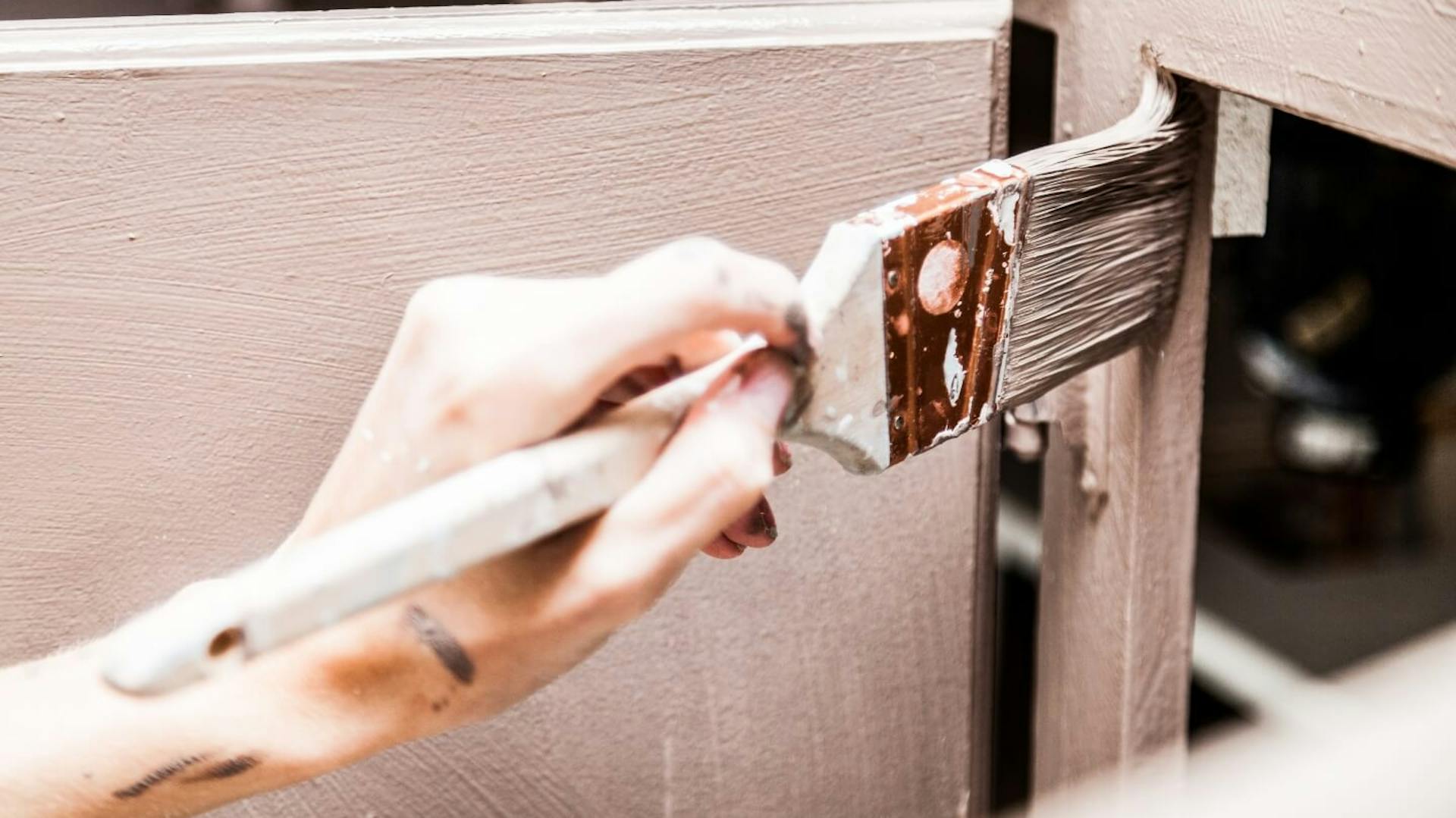 Jemand streicht einen Küchenschrank mit einem Pinsel.