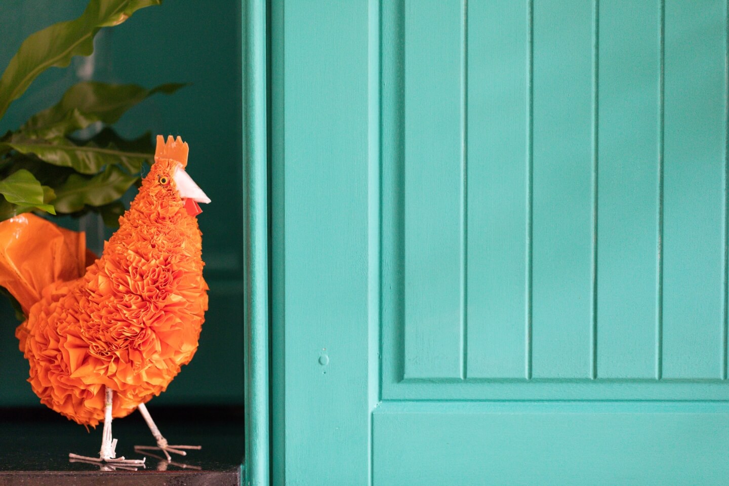 Küchenschrank in türkis mit orangenem Dekohuhn daneben.