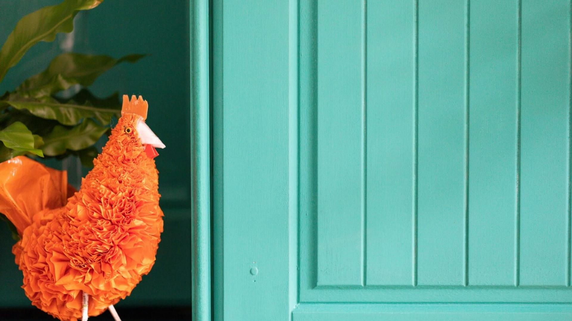 Küchenschrank in türkis mit orangenem Dekohuhn daneben.